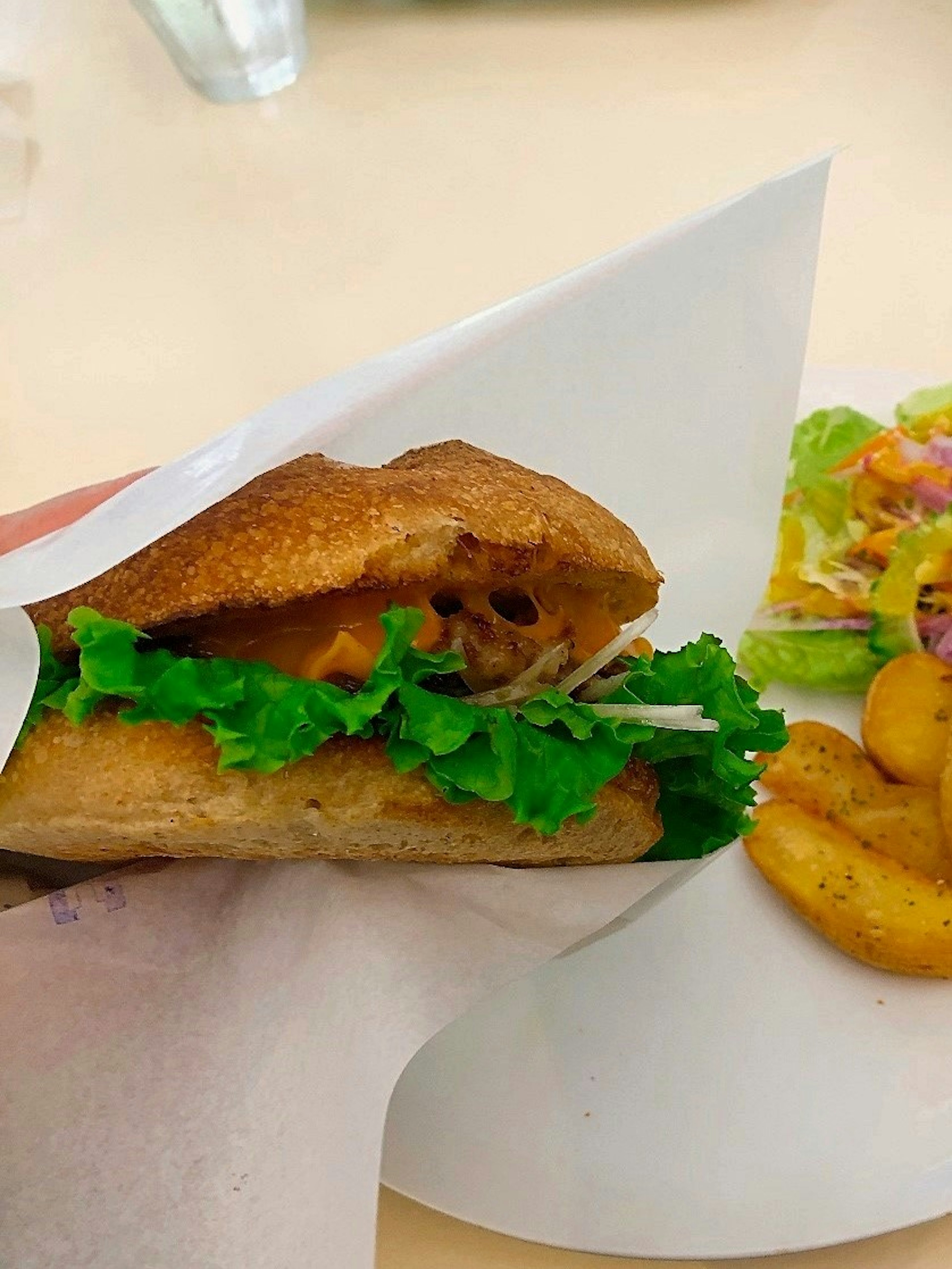 Un sandwich avec de la laitue servi sur une assiette avec une salade d'accompagnement et des quartiers de pommes de terre