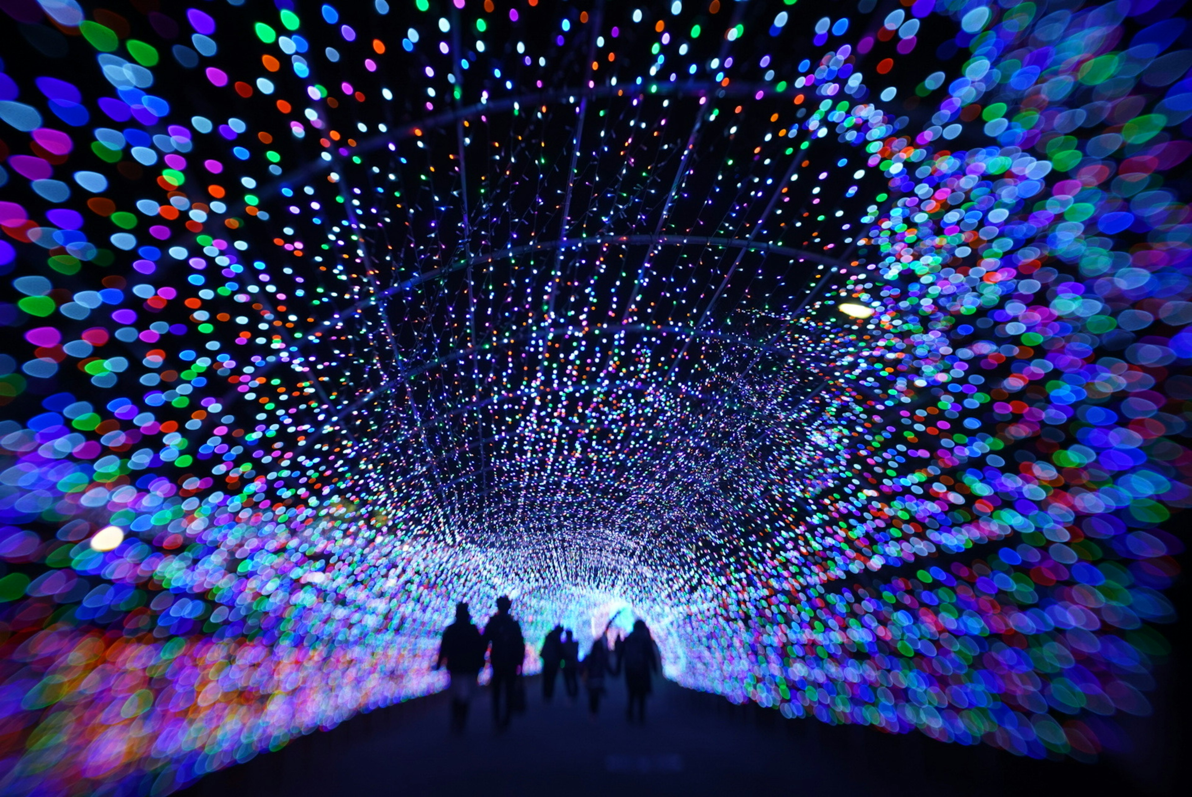 Siluetas de personas caminando bajo un túnel de luces coloridas