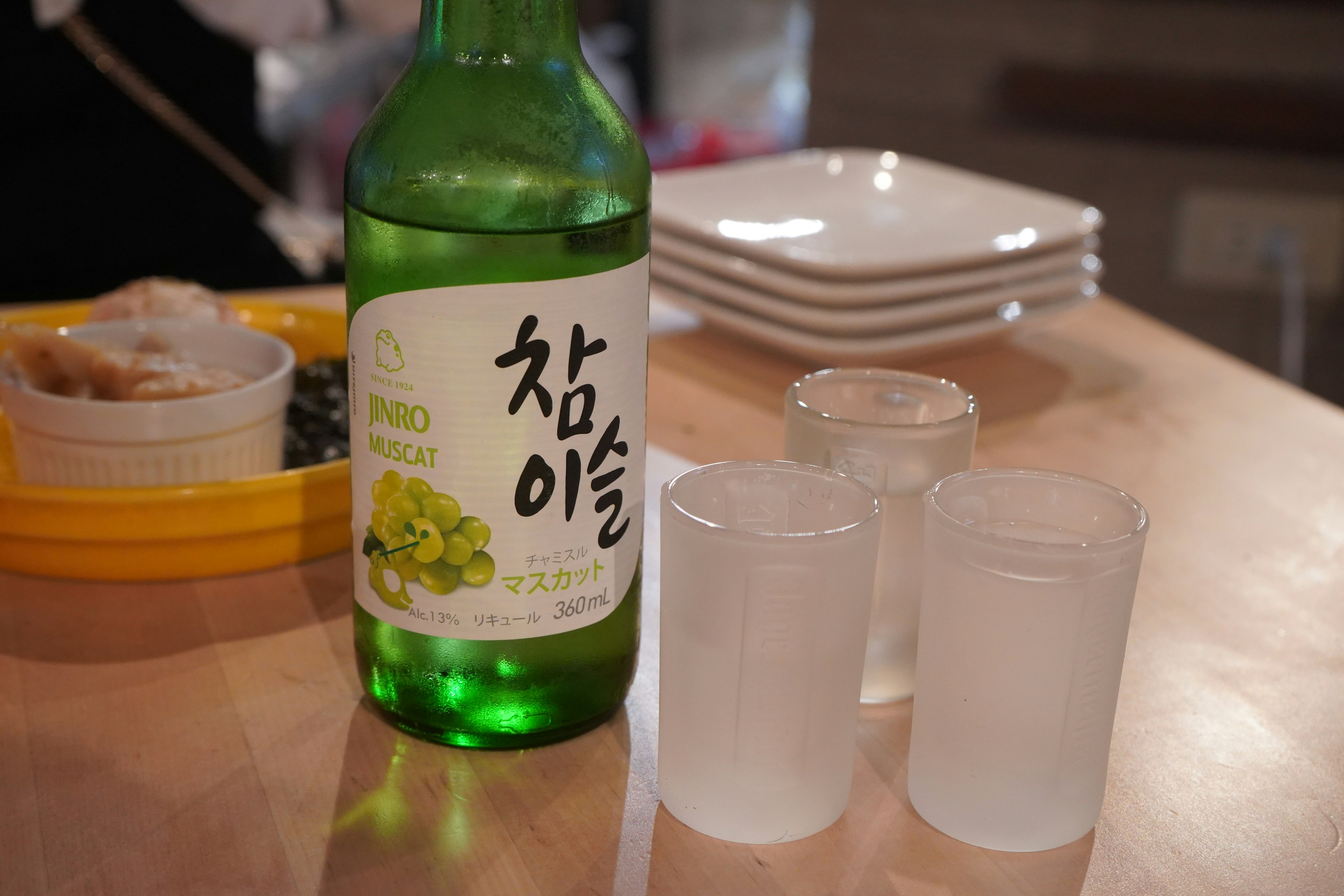 A green bottle of Korean soju with three transparent shot glasses on a table