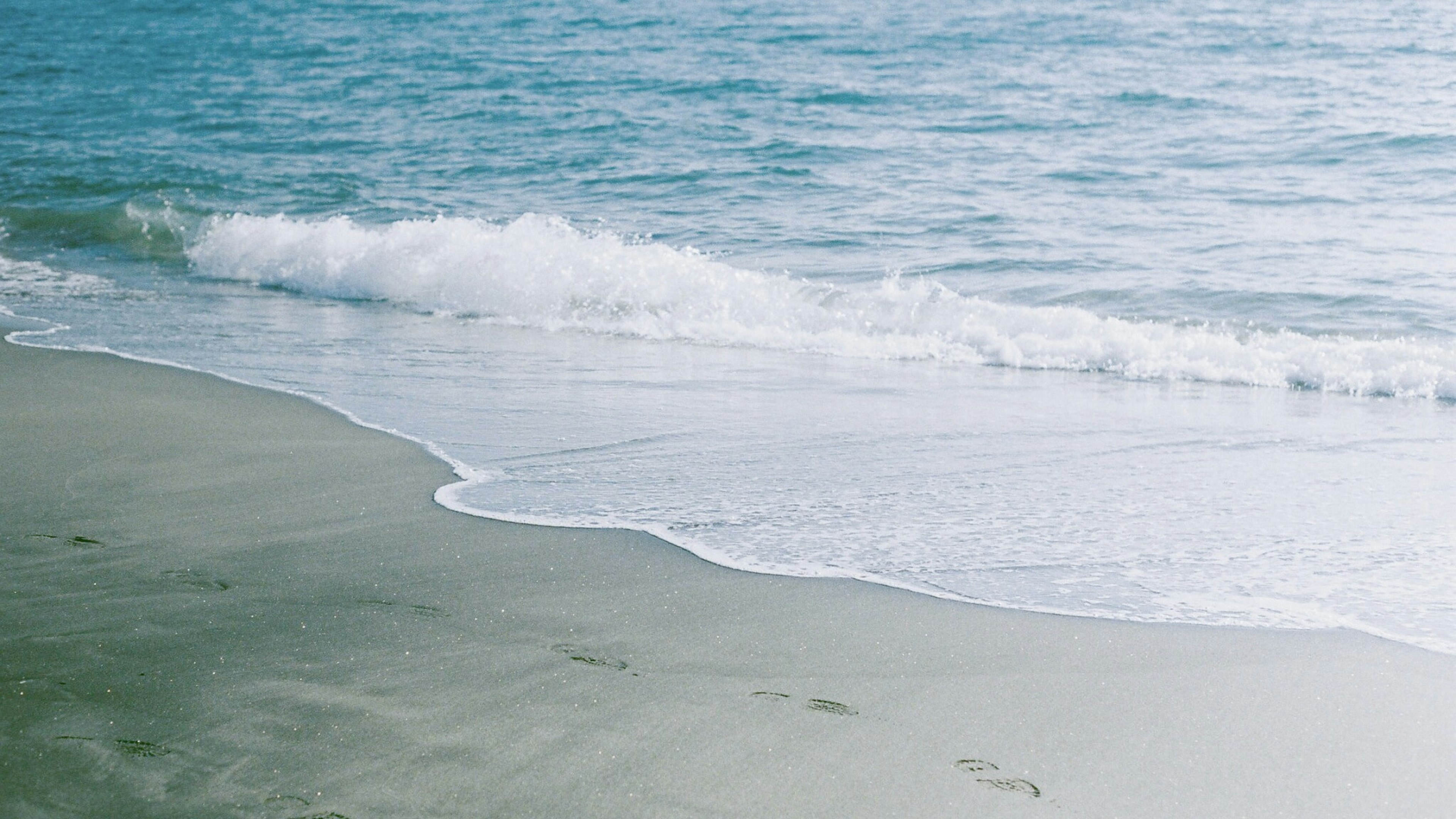 Huellas en una playa de arena con olas suaves