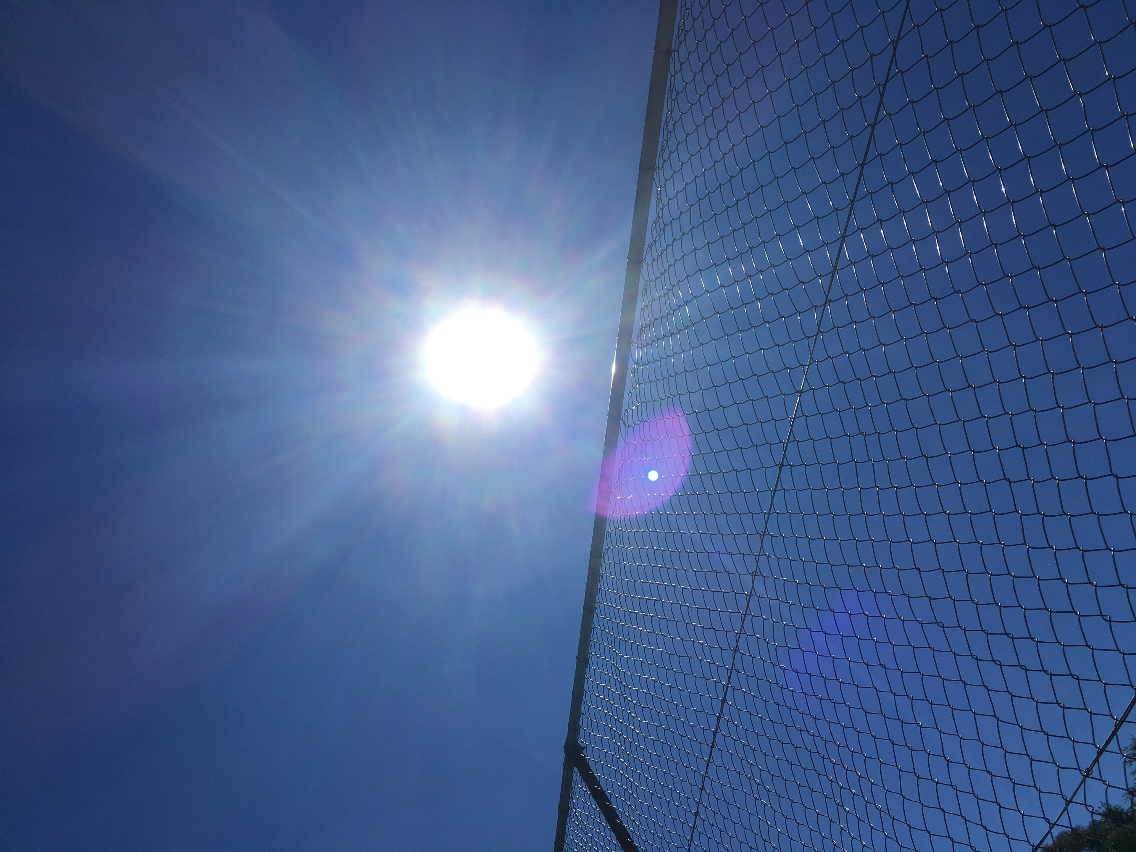 Sol brillante con rayos contra un cielo azul claro y una sección de una red