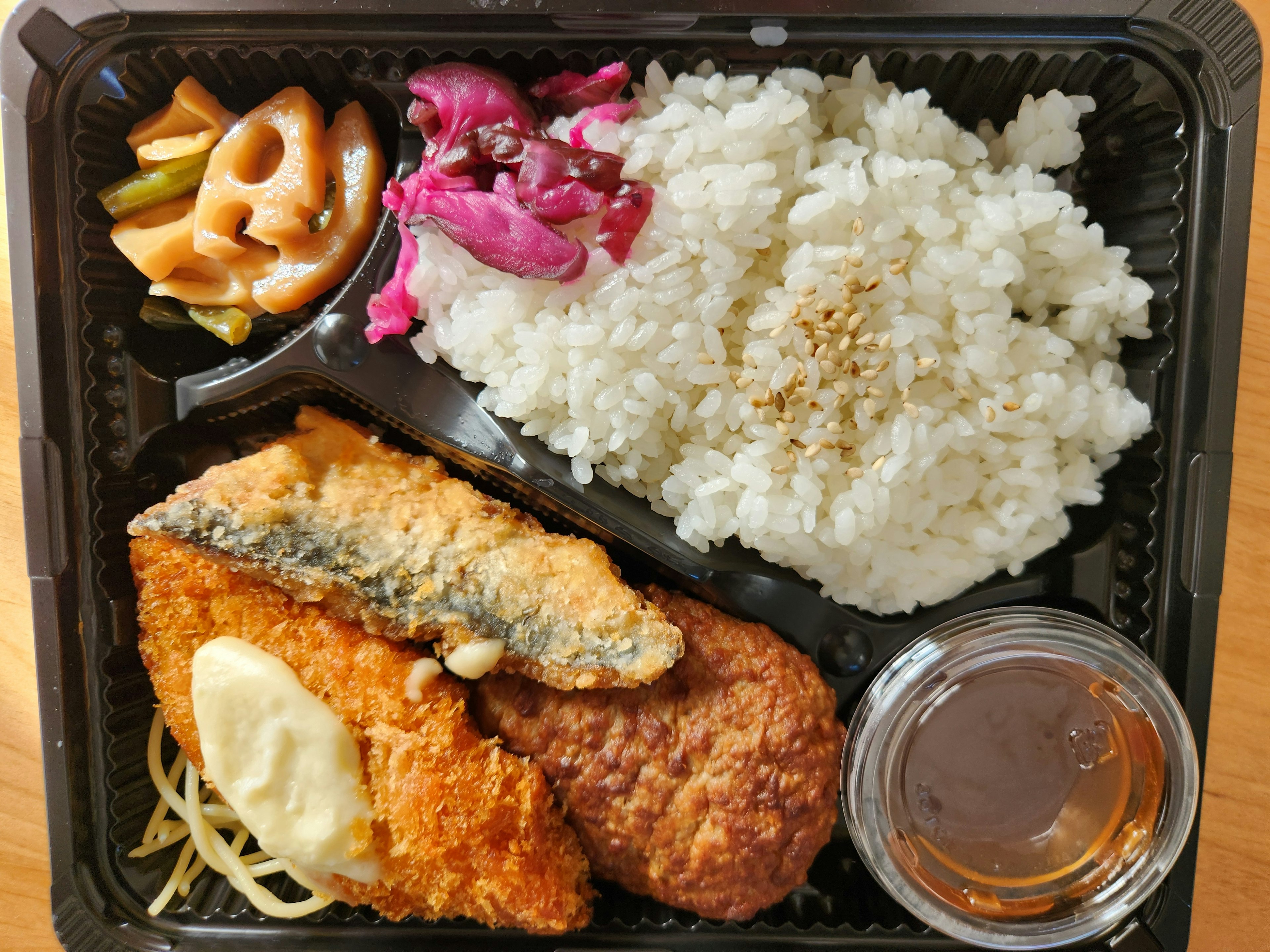 A bento box featuring fried fish, rice, pickled vegetables, and dipping sauce