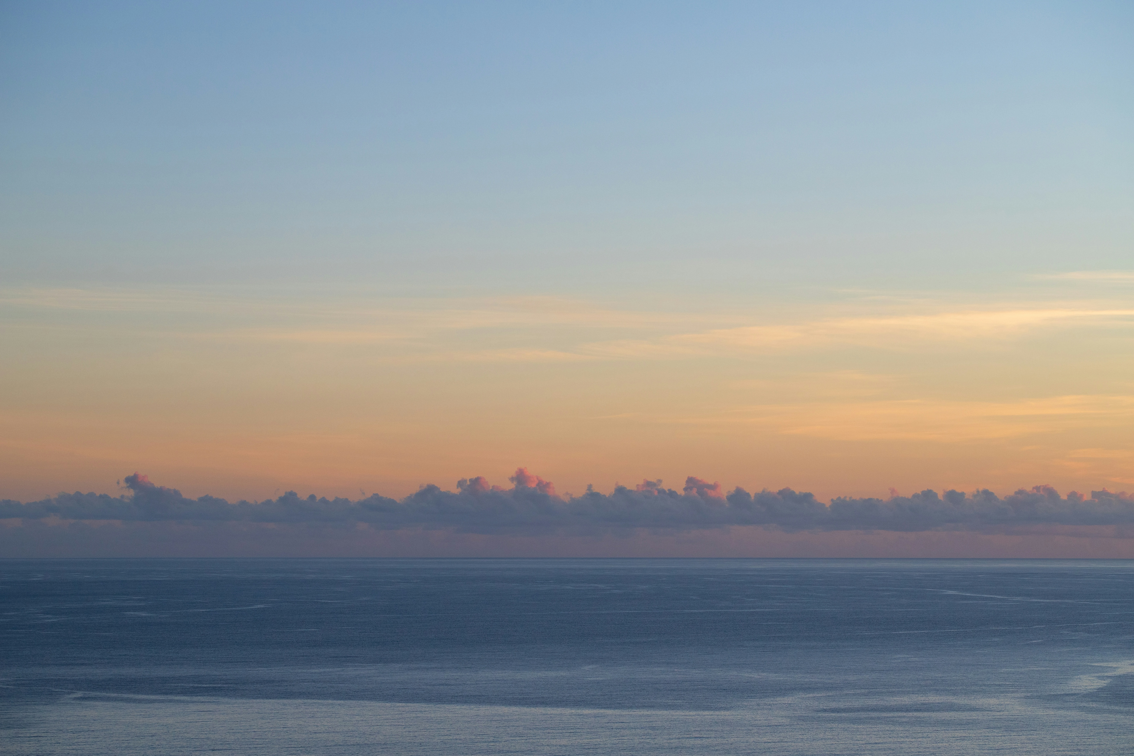 Panoramic view of a calm sea under a pastel sky with orange clouds