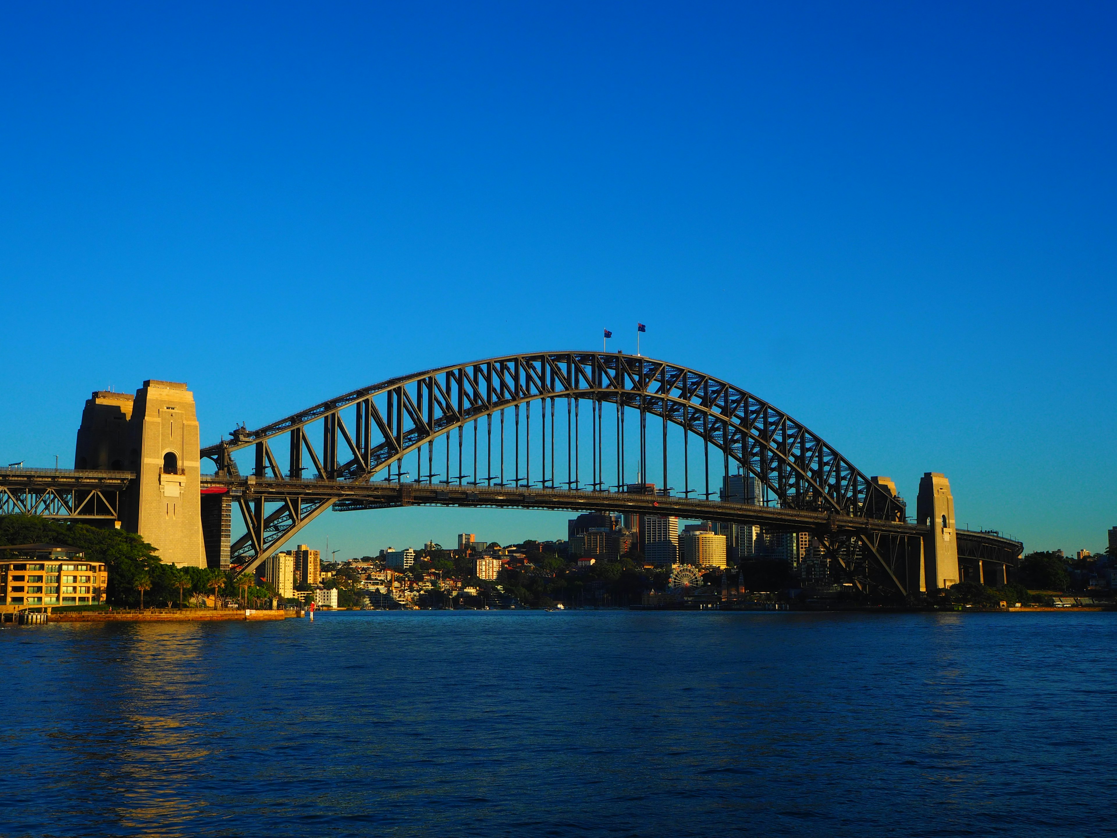 Pemandangan Jembatan Pelabuhan Sydney di bawah langit biru cerah dengan garis cakrawala kota