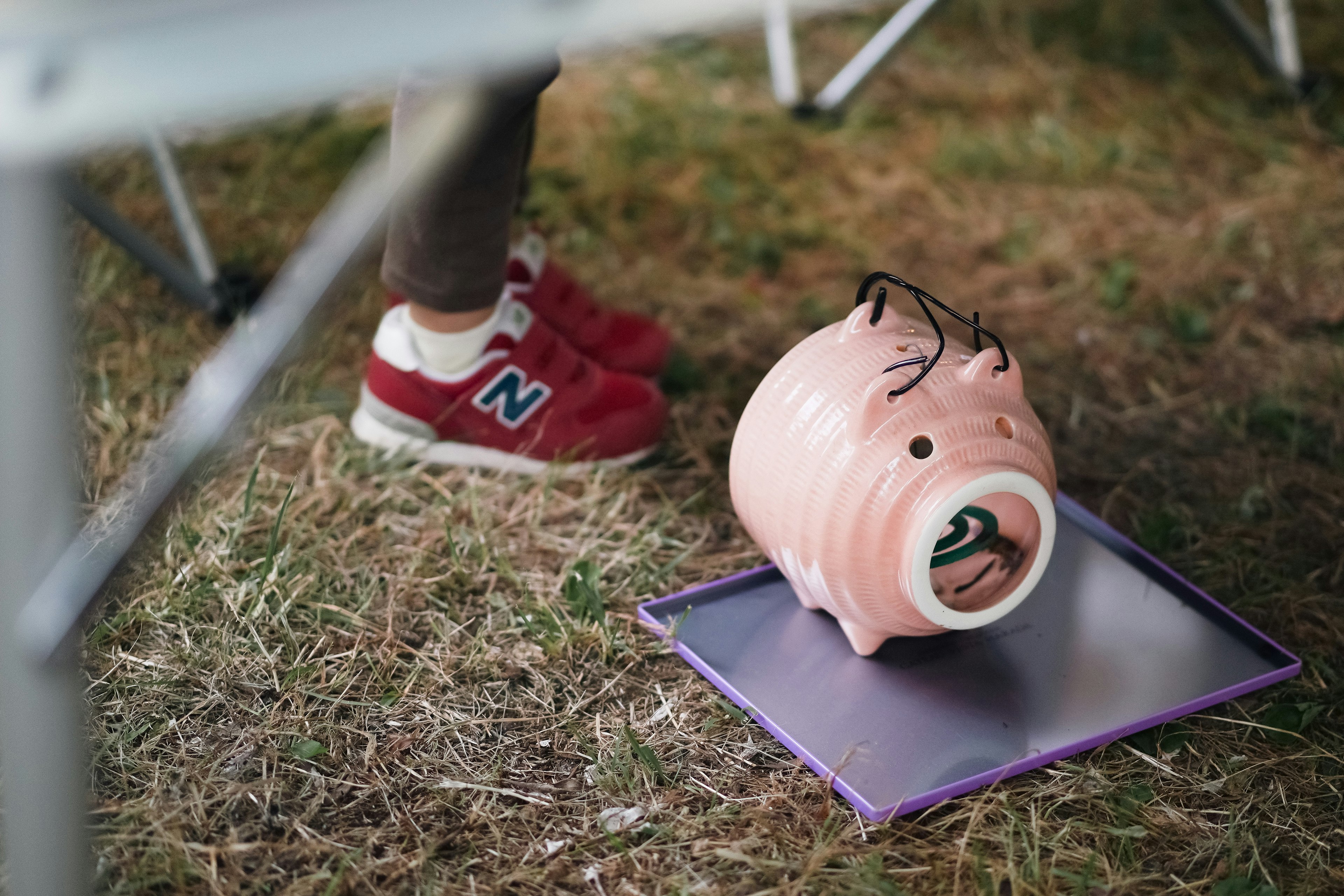 A pink piggy bank tipped over on a purple surface near a foot wearing red New Balance shoes