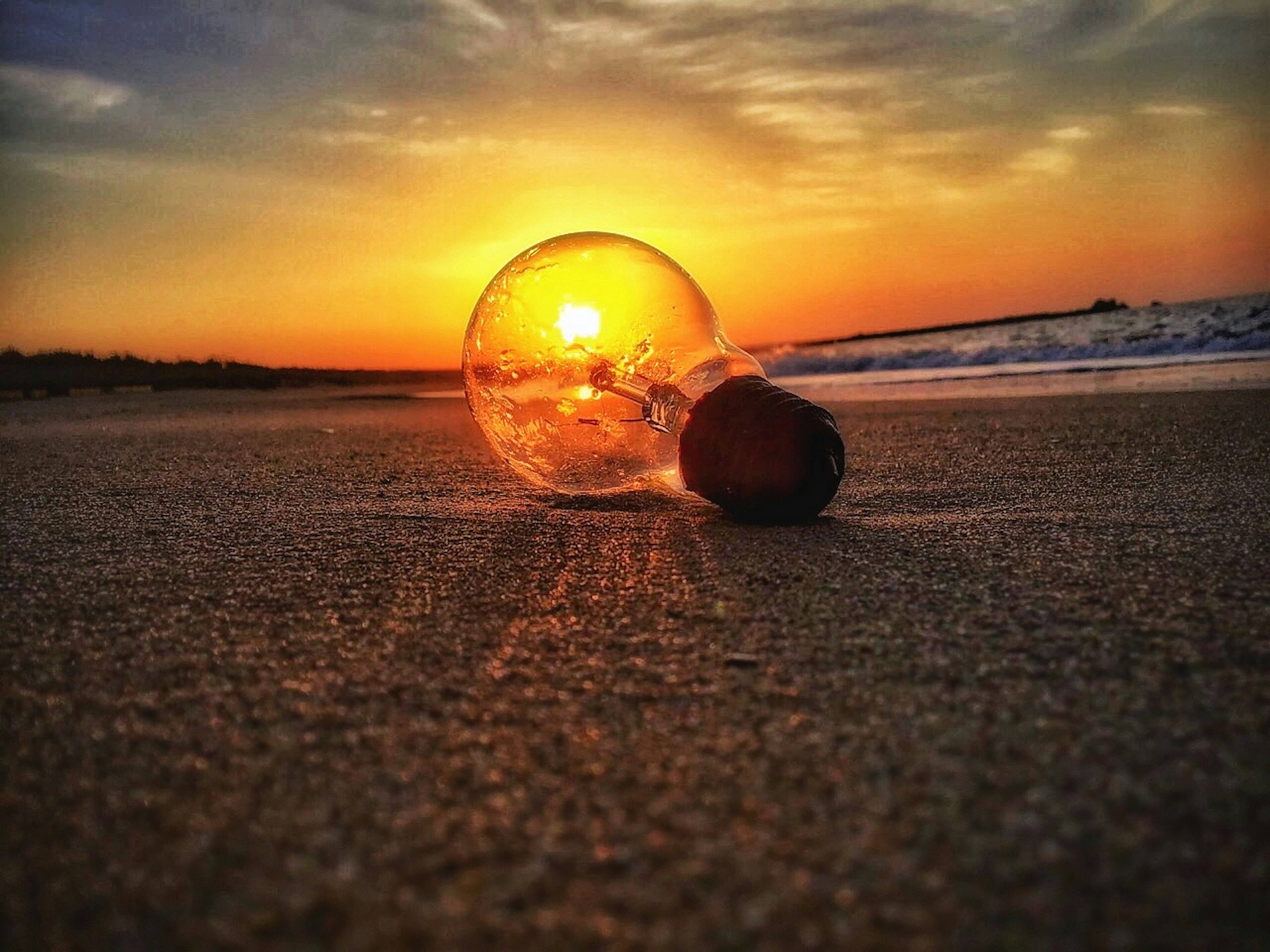 Una bombilla reflejando el atardecer en una playa de arena