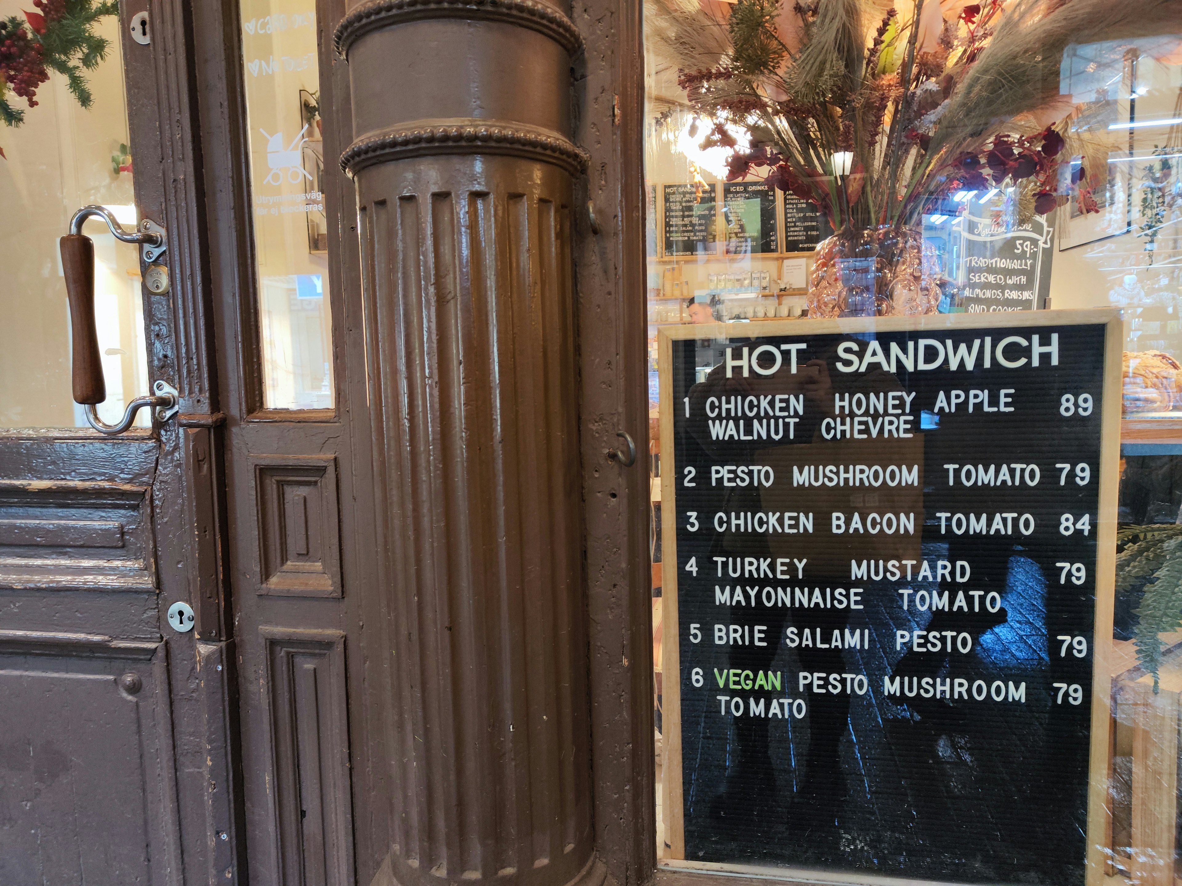 Un exterior de café con un cartel de menú de sándwich caliente y una columna de madera