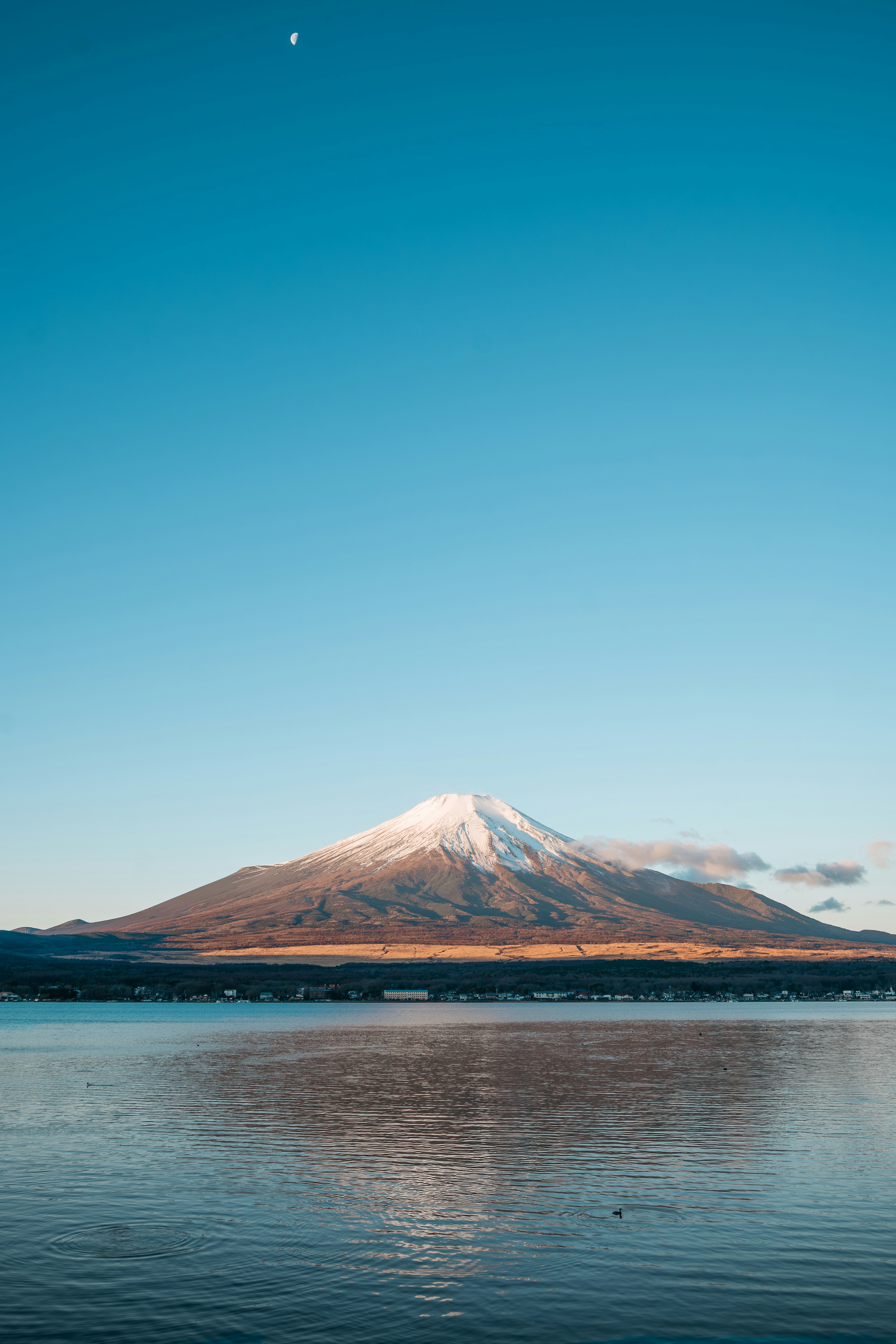 Snow-capped mountain reflecting in calm water under a clear blue sky