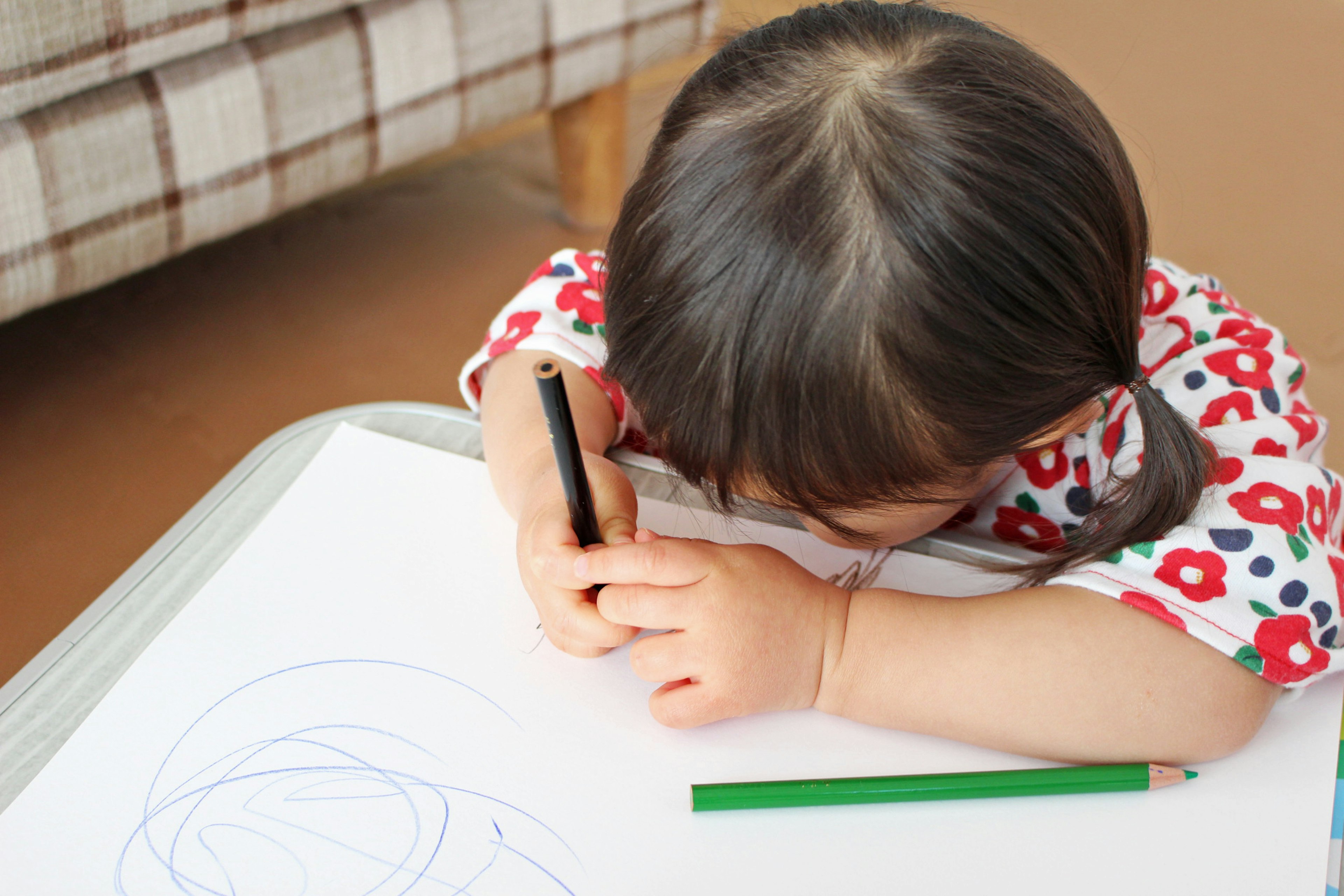 Anak menggambar di kertas mengenakan baju bermotif bunga