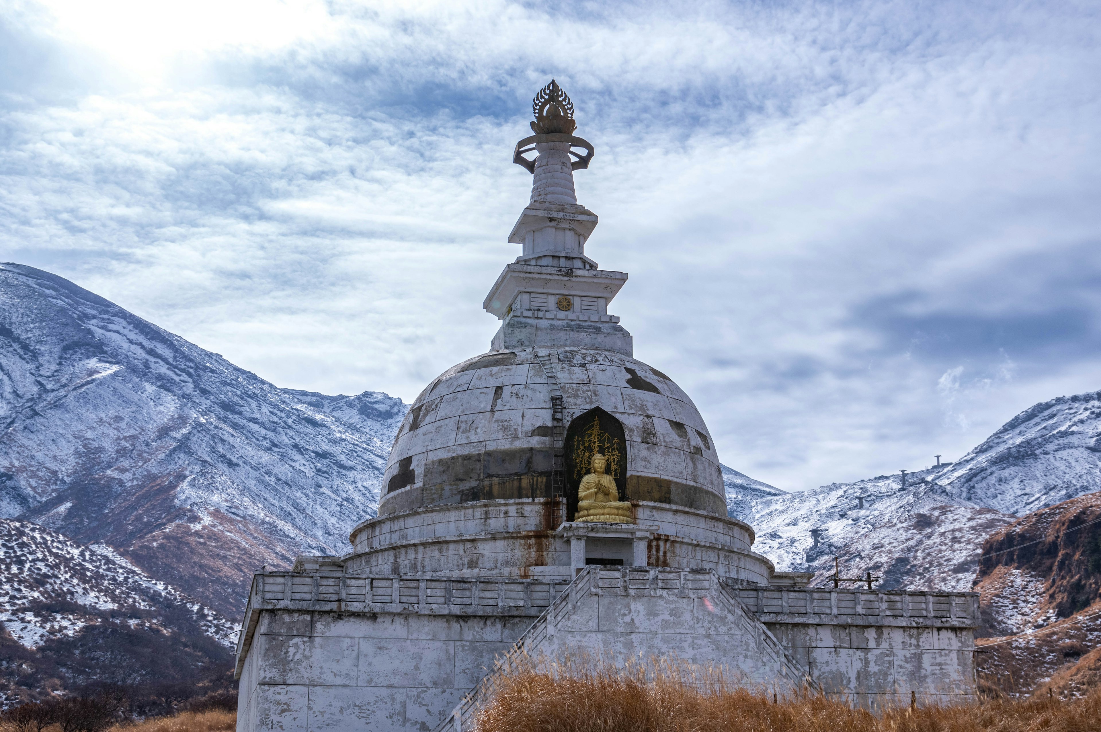 Stupa bianca con una statua di Buddha dorata circondata da montagne innevate