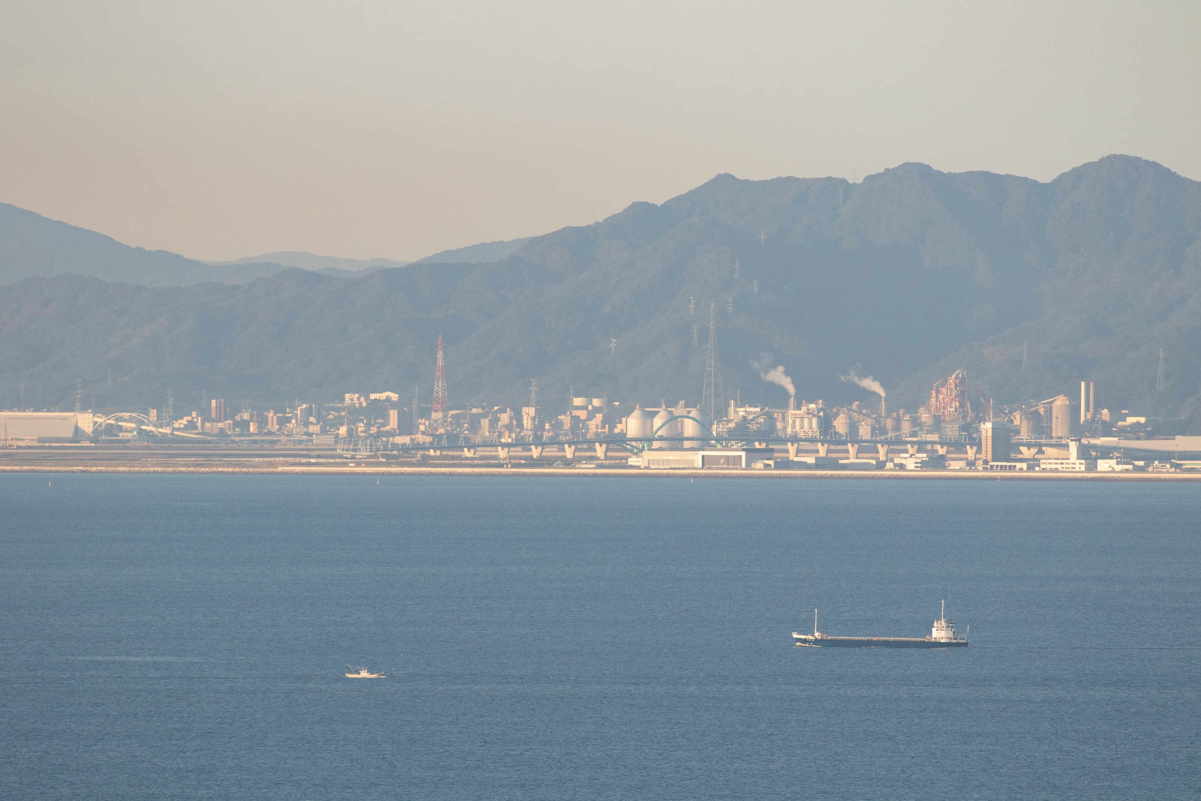 Paisaje urbano con montañas al fondo gran barco y pequeño bote en el agua