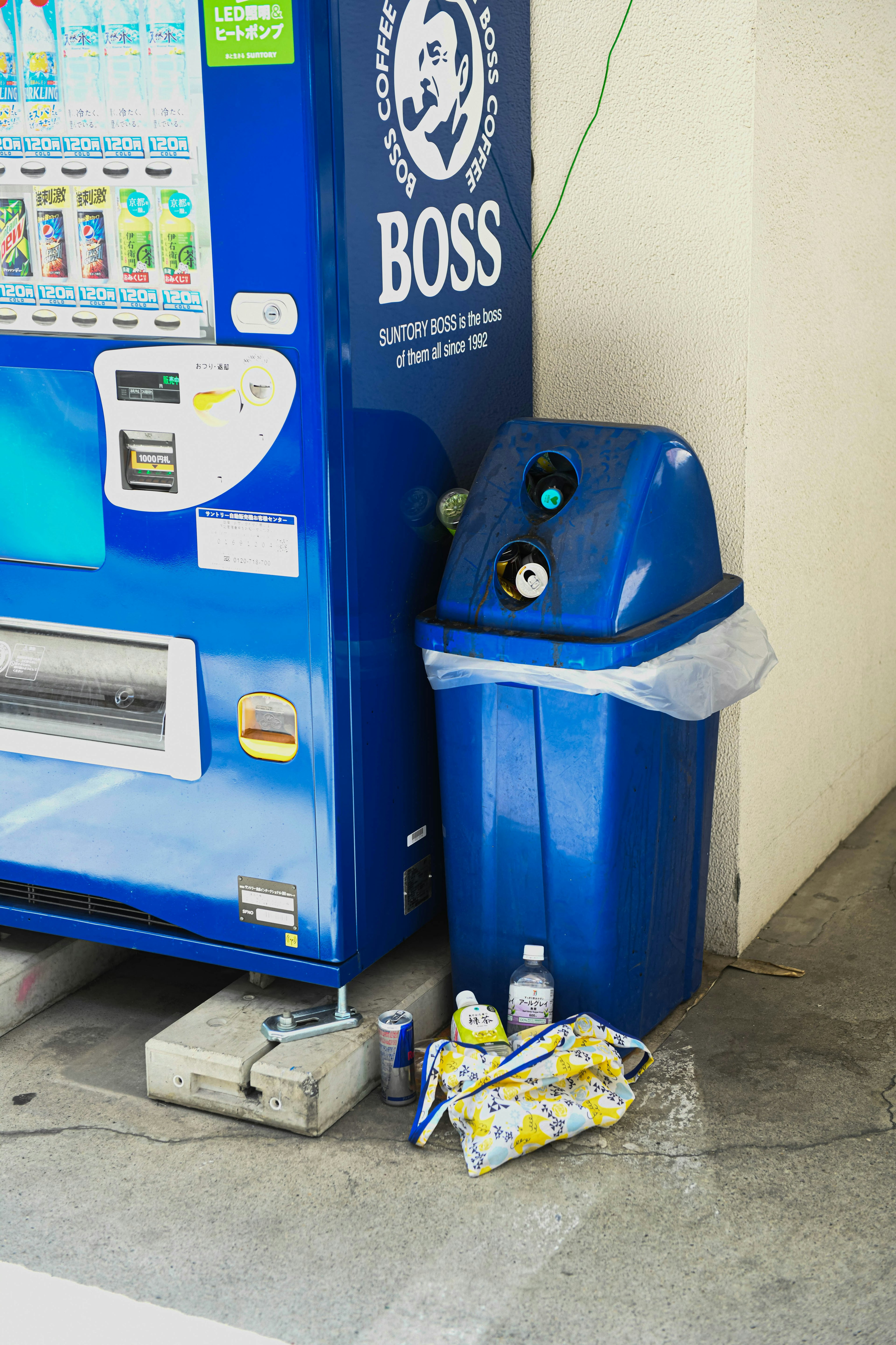 Scene with a vending machine and a blue trash can Bottles and wrappers placed nearby