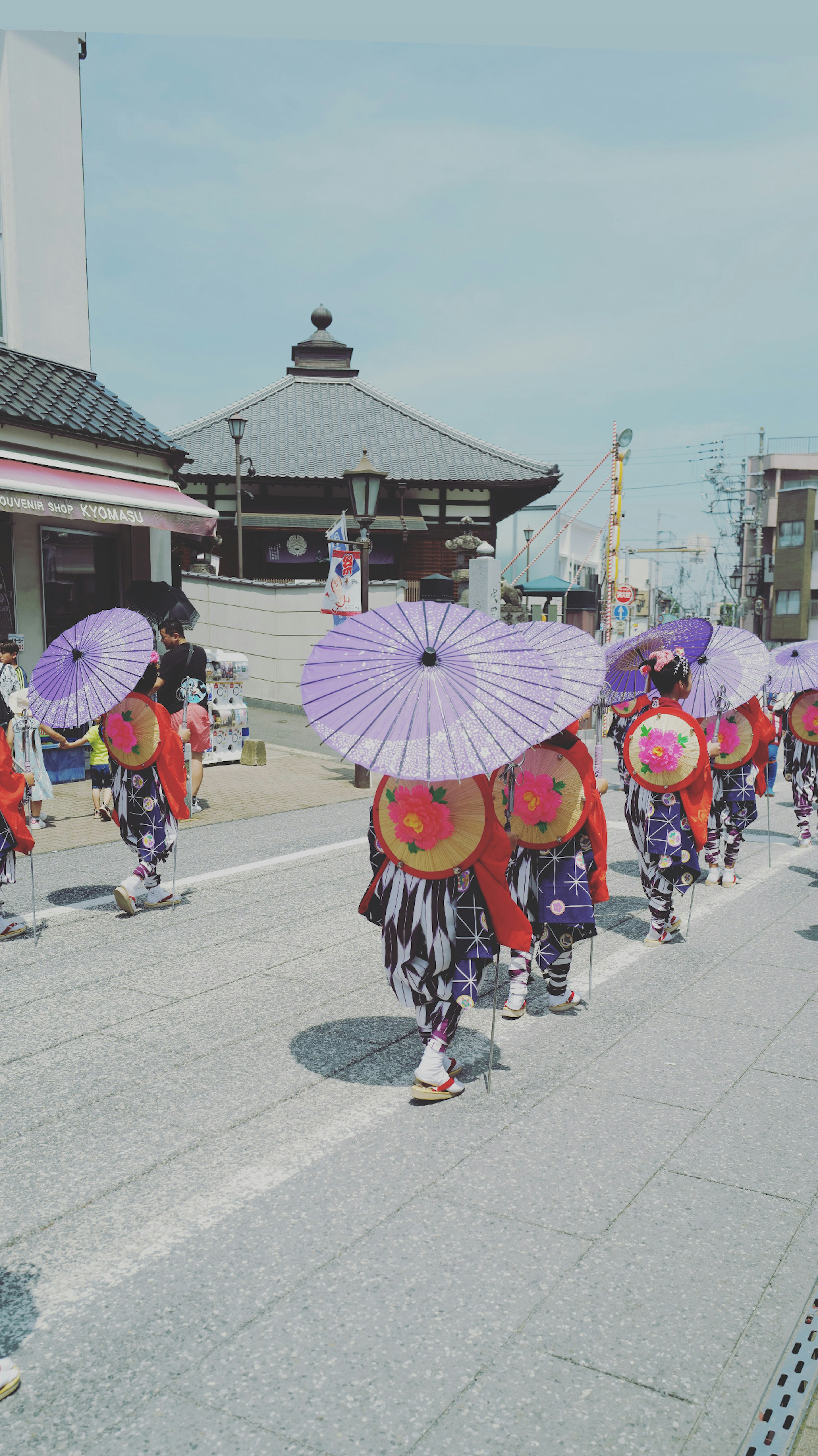 Dancers holding purple umbrellas walking in a festival setting