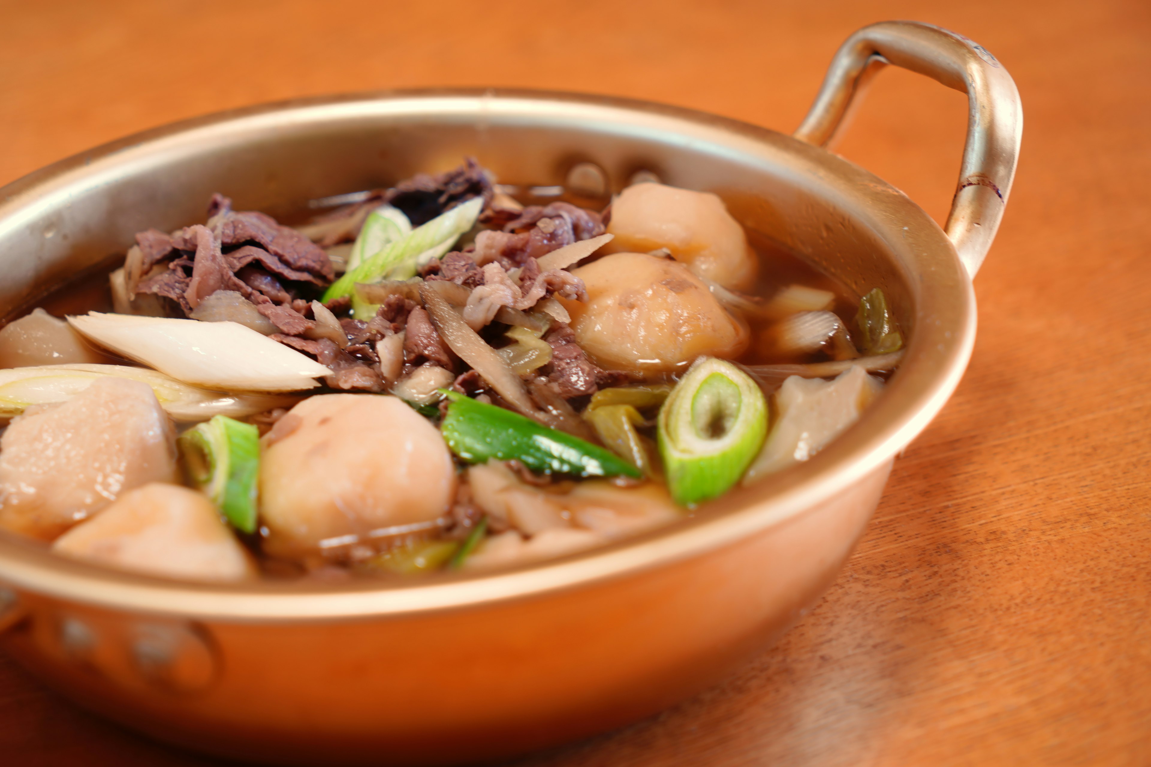 Hidangan sup dalam mangkuk emas dengan bakso dan irisan daun bawang