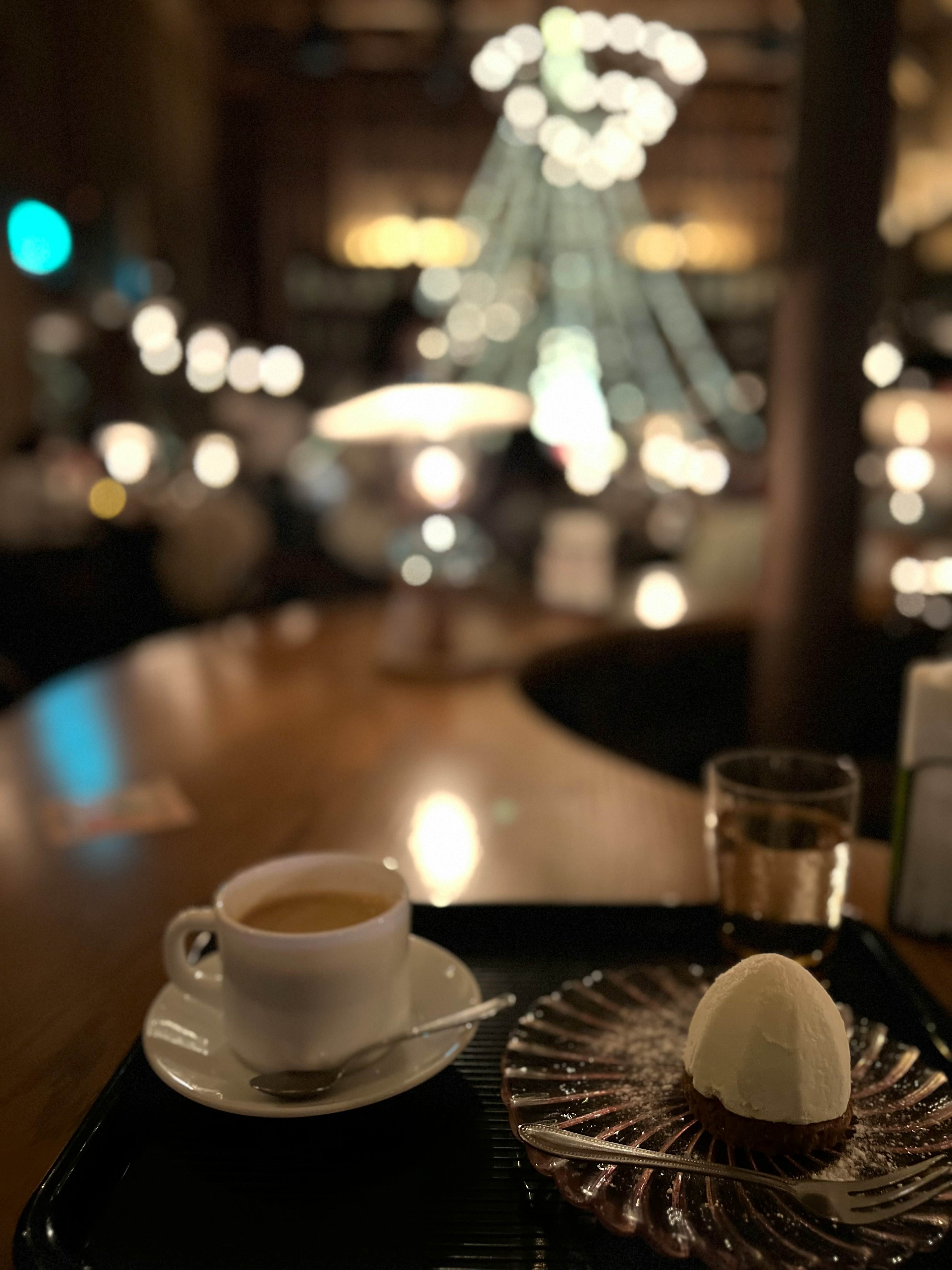 A coffee cup and dessert on a tray with a softly lit cafe background