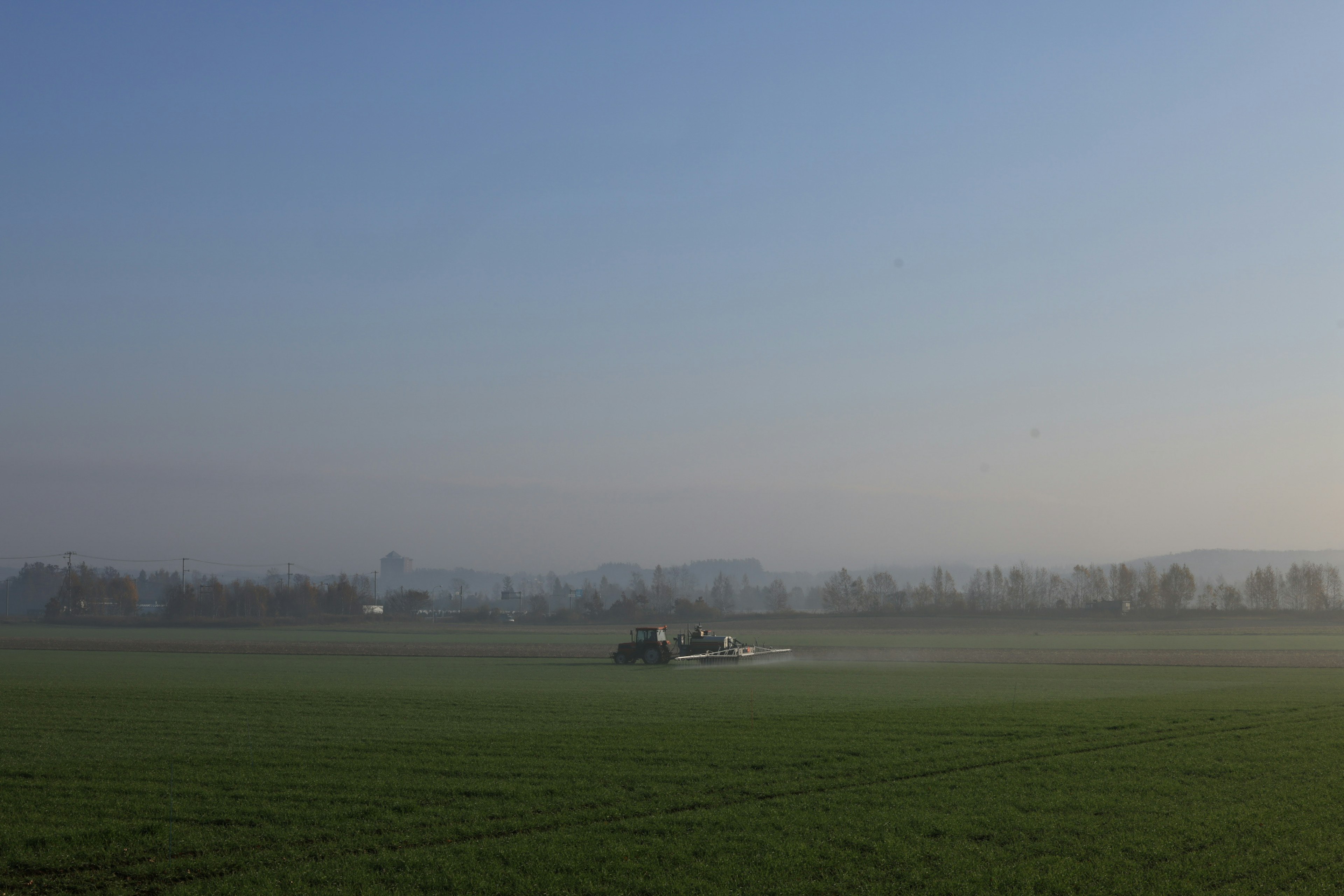 Trattore che ara un campo nebbioso sotto un cielo blu