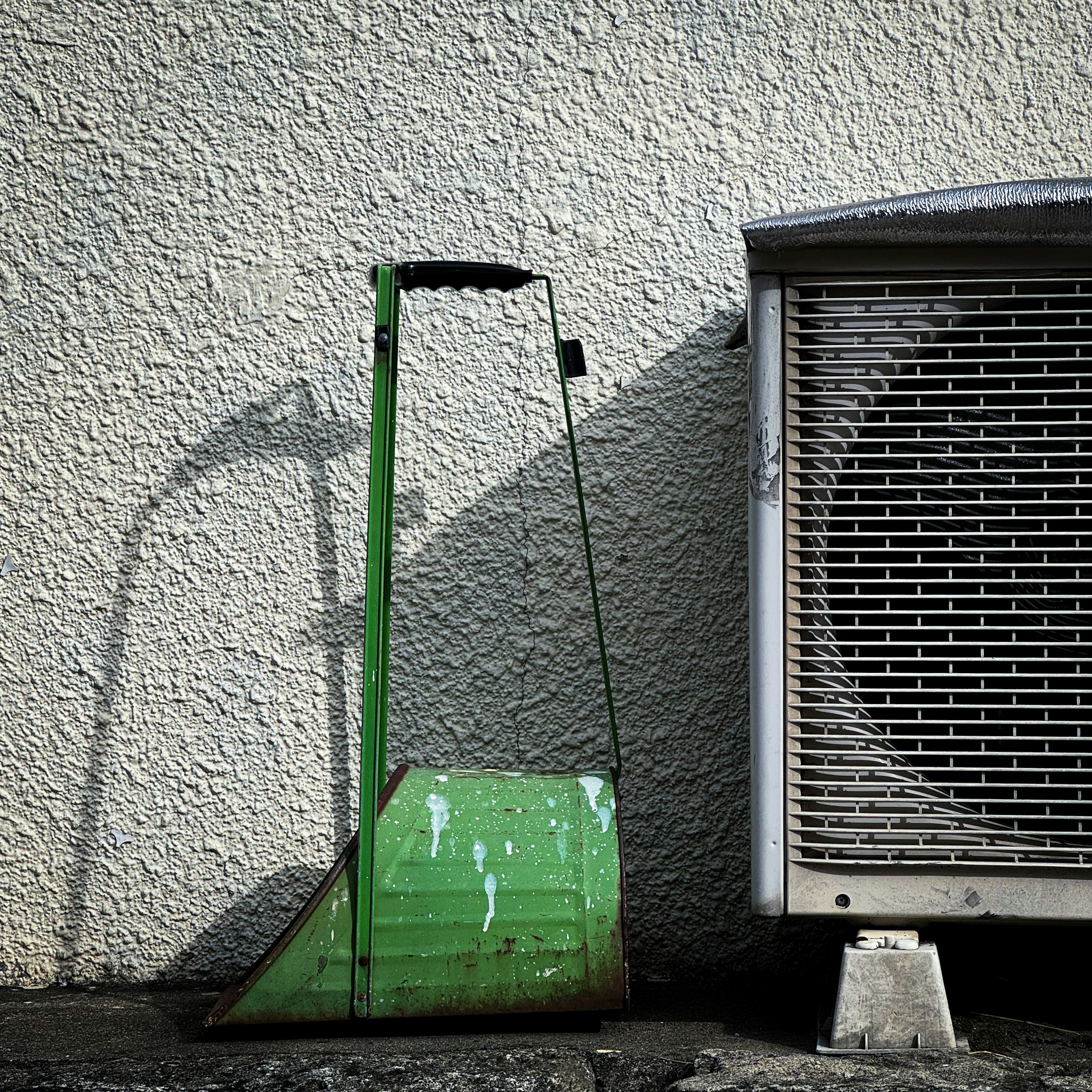 Una pala verde desgastada al lado de una unidad de aire acondicionado contra una pared texturizada