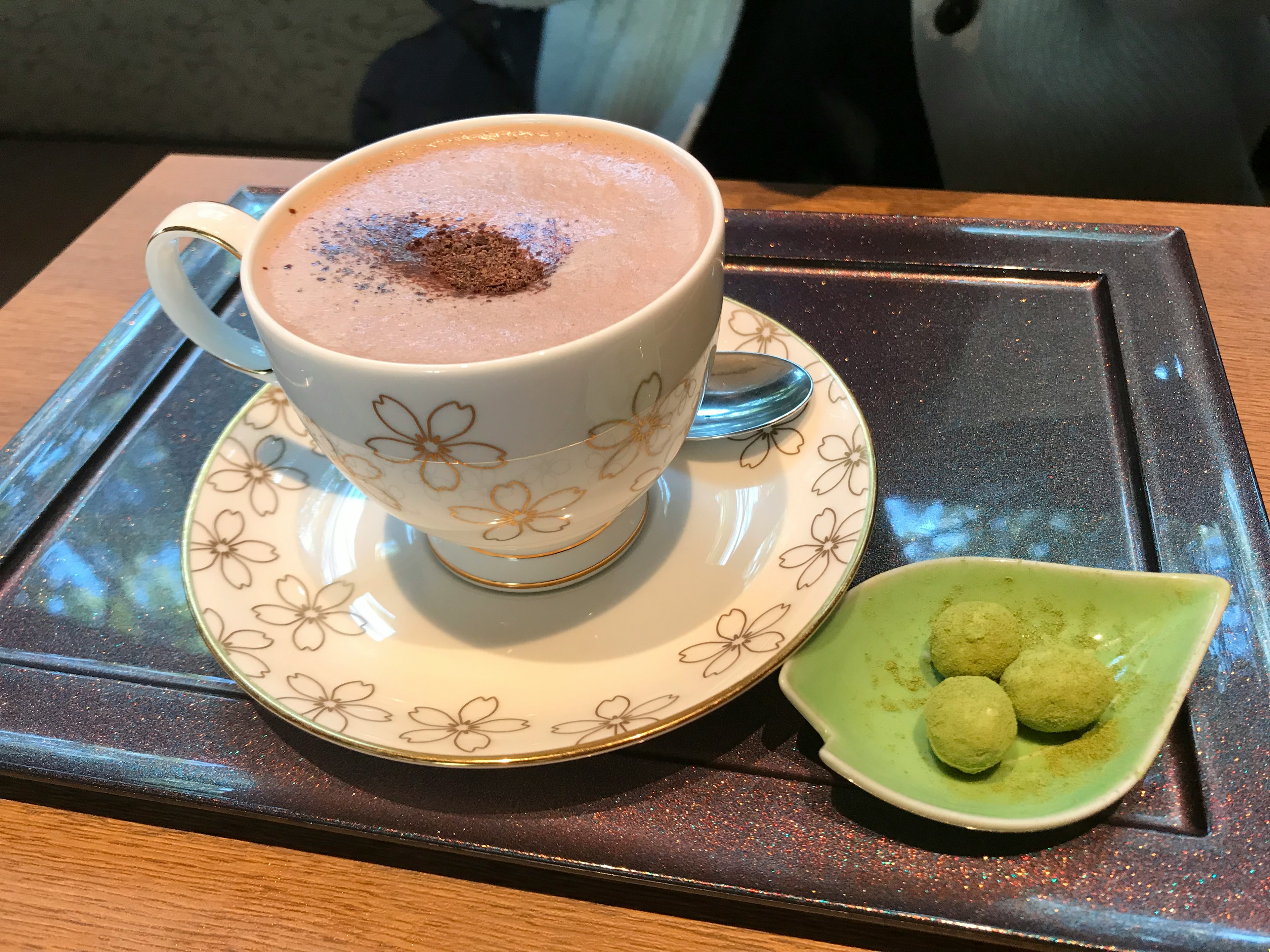 Cioccolata calda in una tazza bianca con motivi floreali e dolci al matcha su un piatto verde