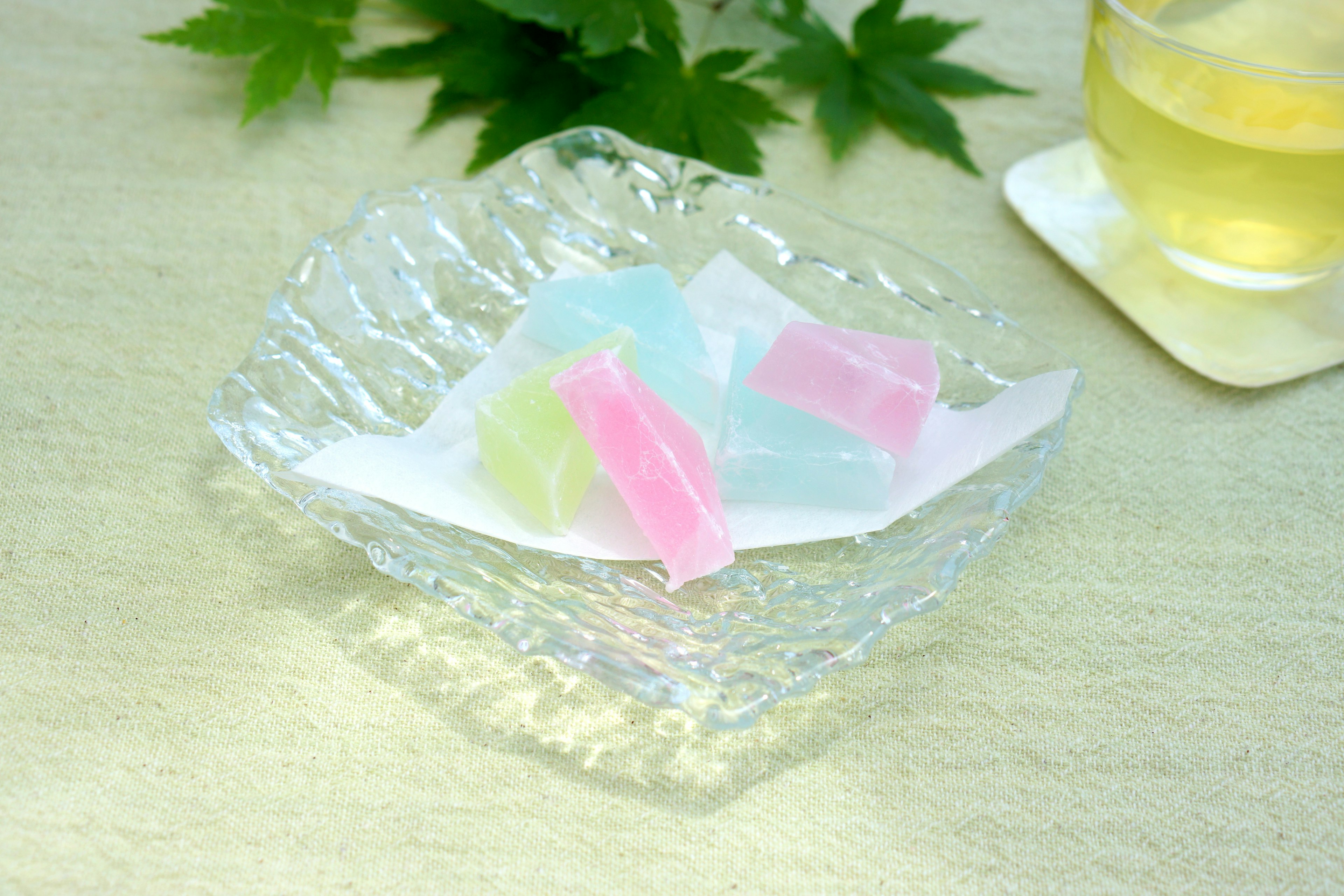 Dulces japoneses coloridos en un plato de vidrio transparente con una taza de té al fondo