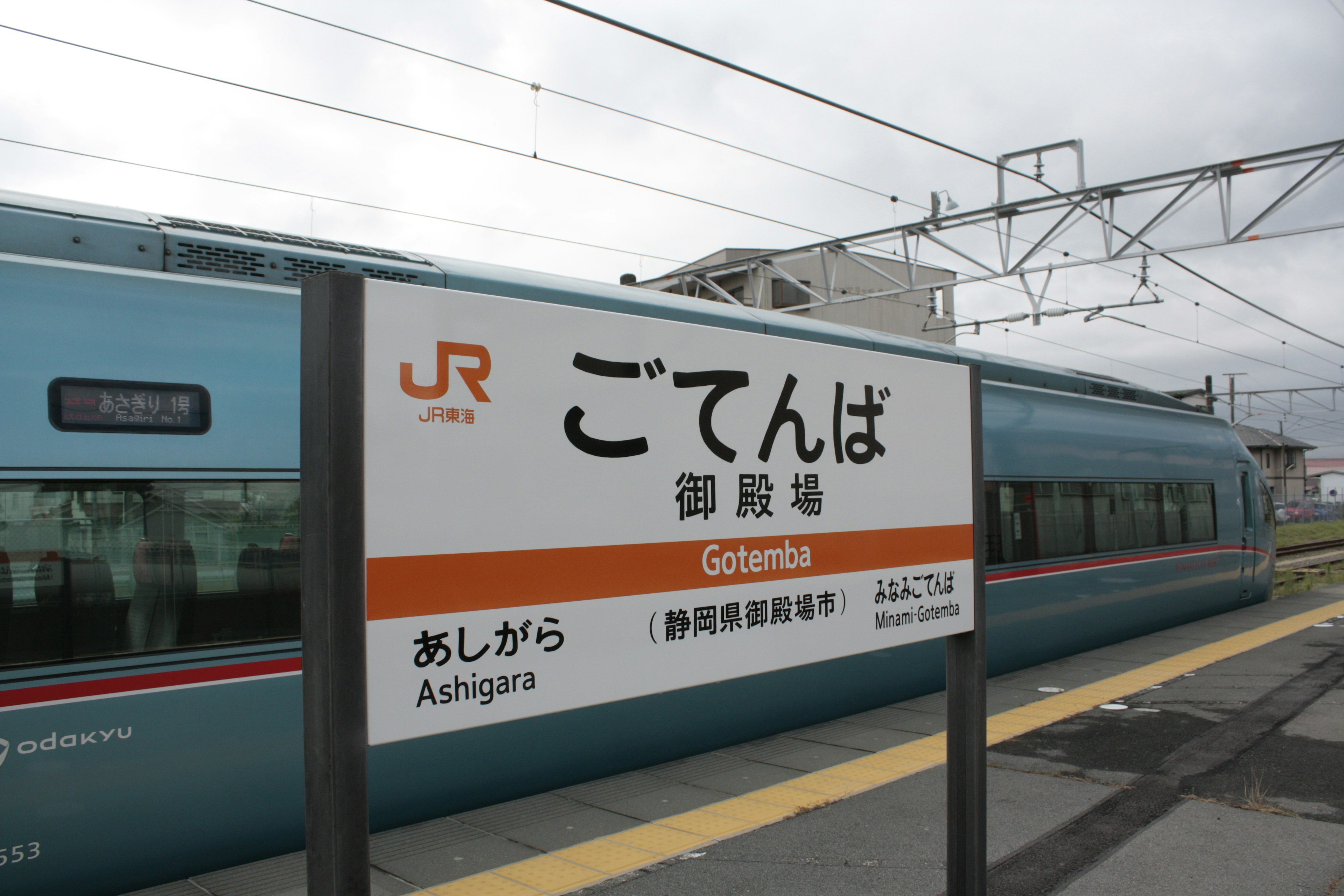 Tanda Stasiun Gotemba dengan kereta biru di latar belakang