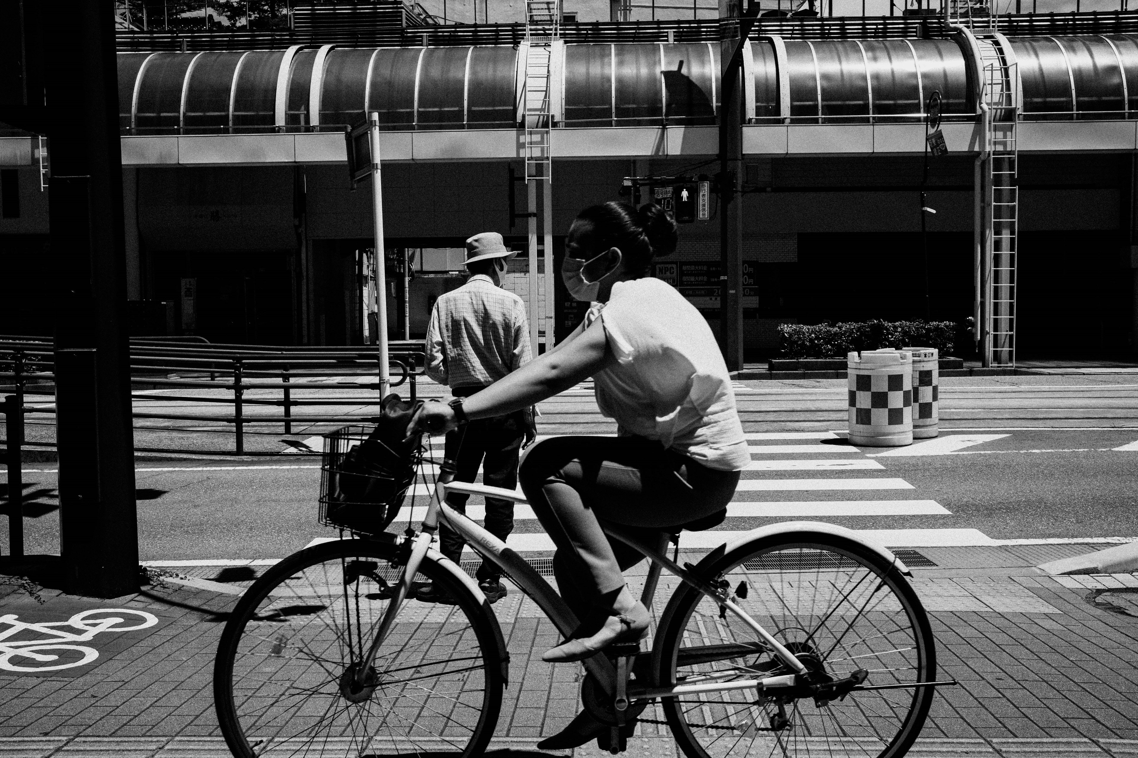 Black and white scene of a woman riding a bicycle and a man walking on the sidewalk