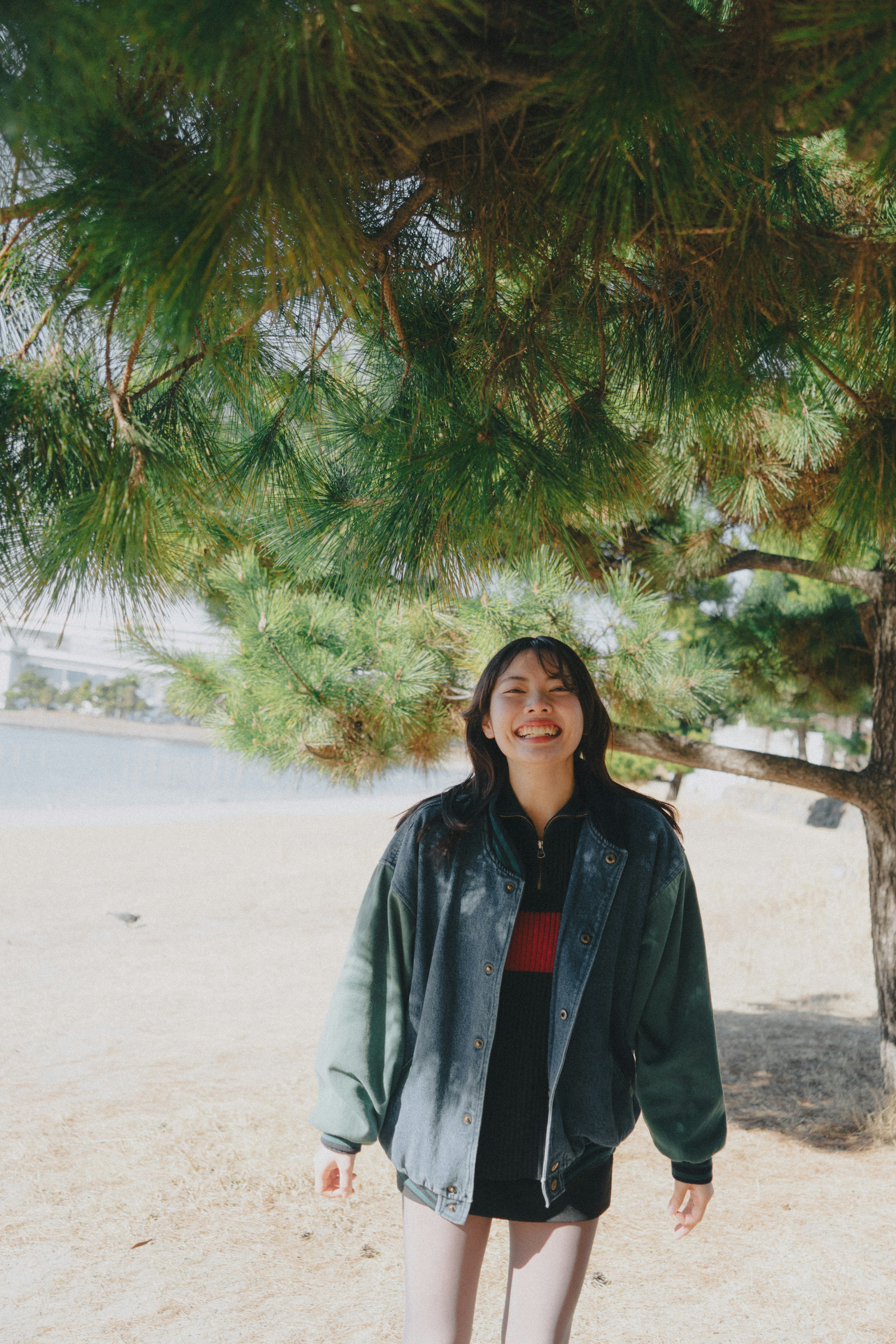 Una mujer sonriente bajo un árbol verde con una gran chaqueta negra