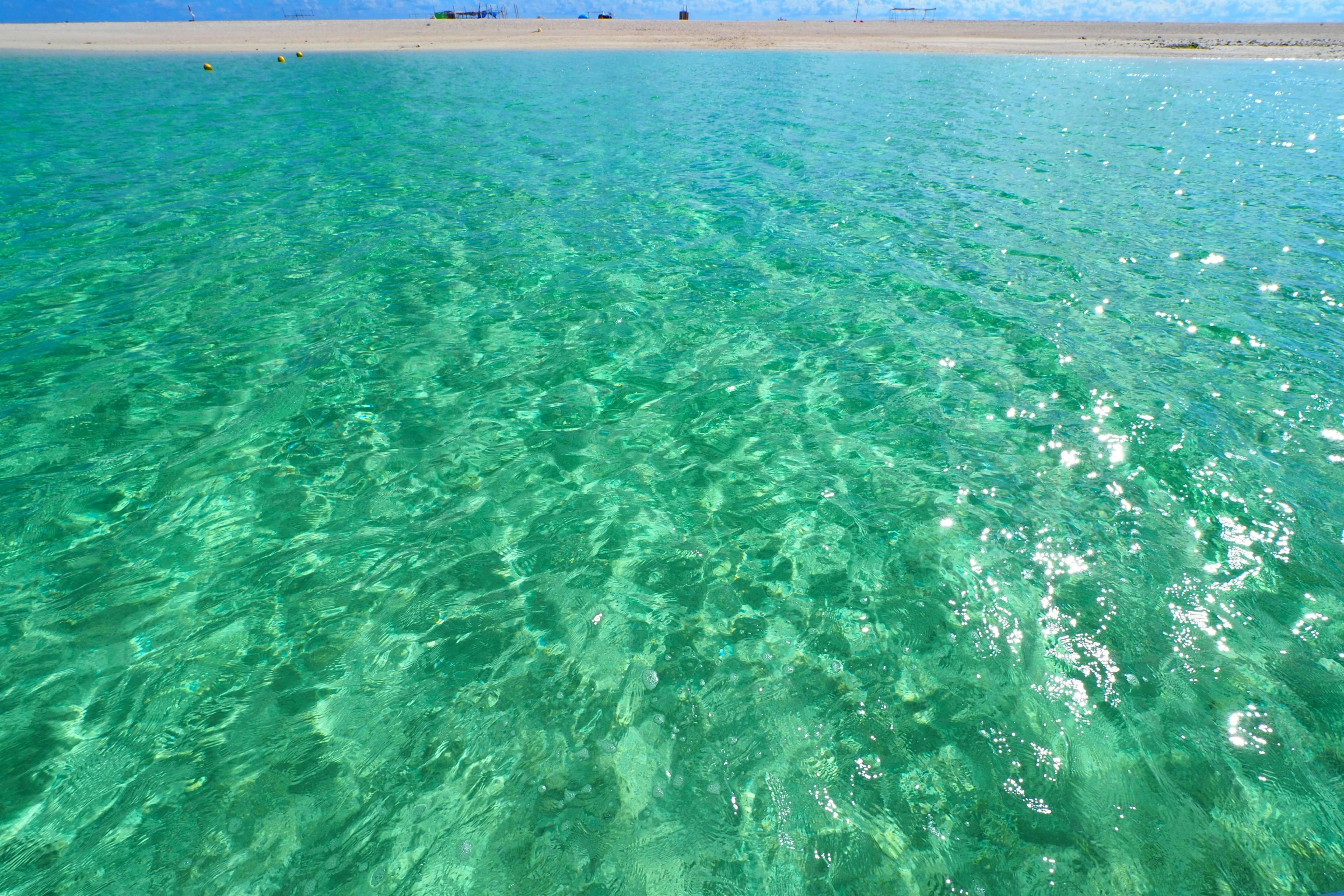 Air laut turquoise yang jelas memantulkan sinar matahari di bawah langit biru