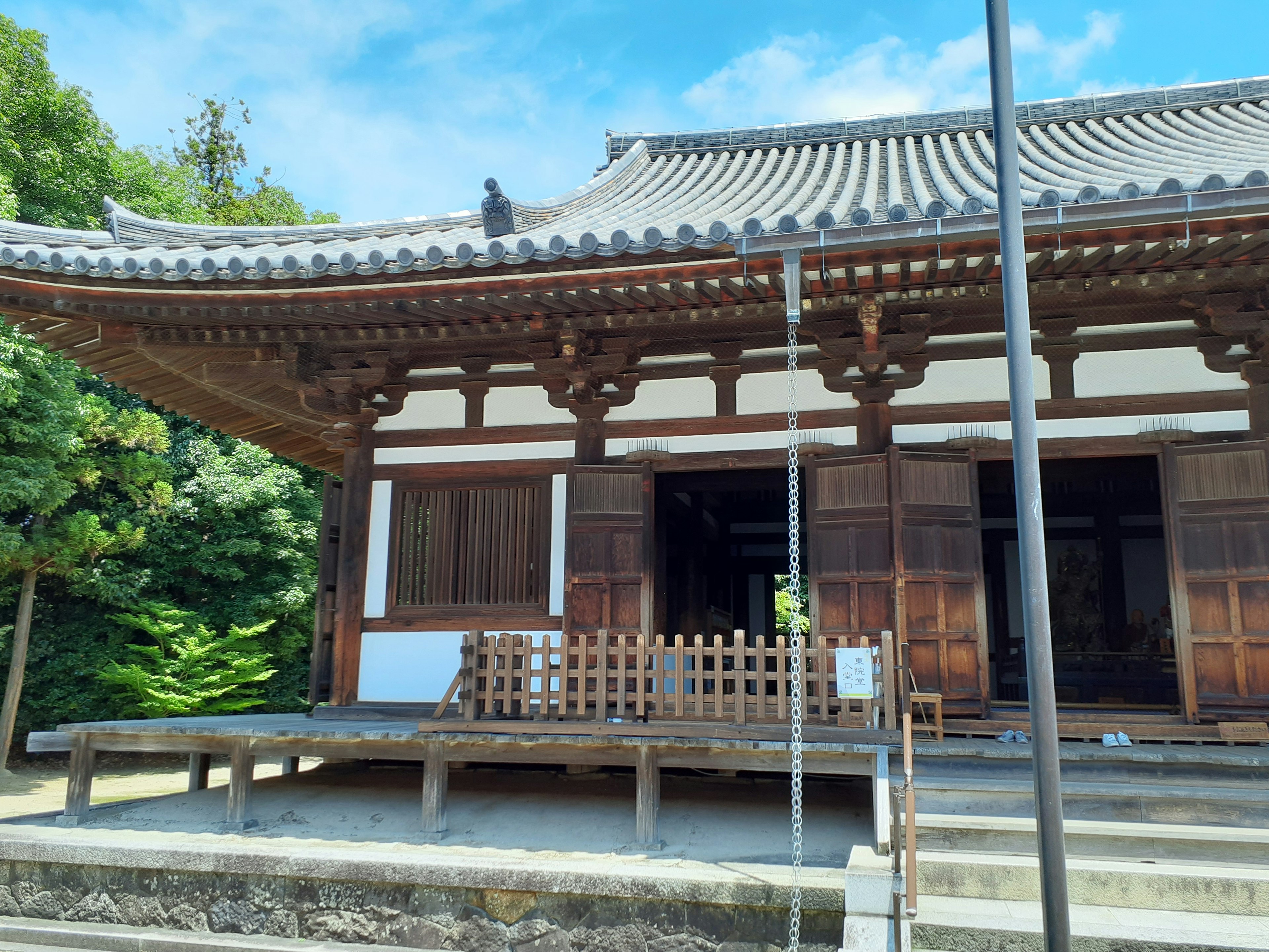 Exterior de un templo japonés tradicional con estructura de madera y techo distintivo rodeado de exuberante vegetación