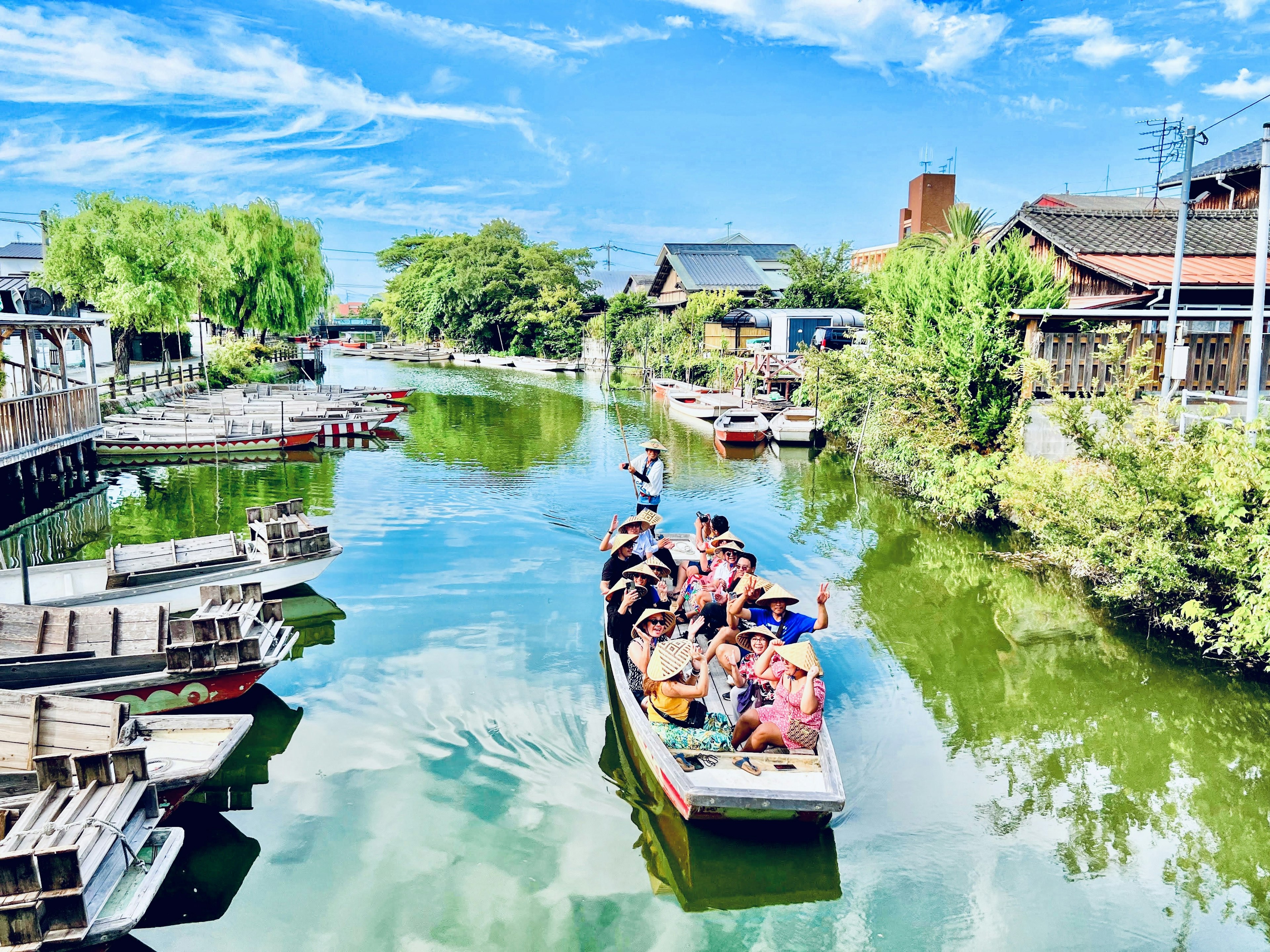 เรือท่องเที่ยวแล่นในคลองใต้ท้องฟ้าสีฟ้าพร้อมต้นไม้เขียวชอุ่ม