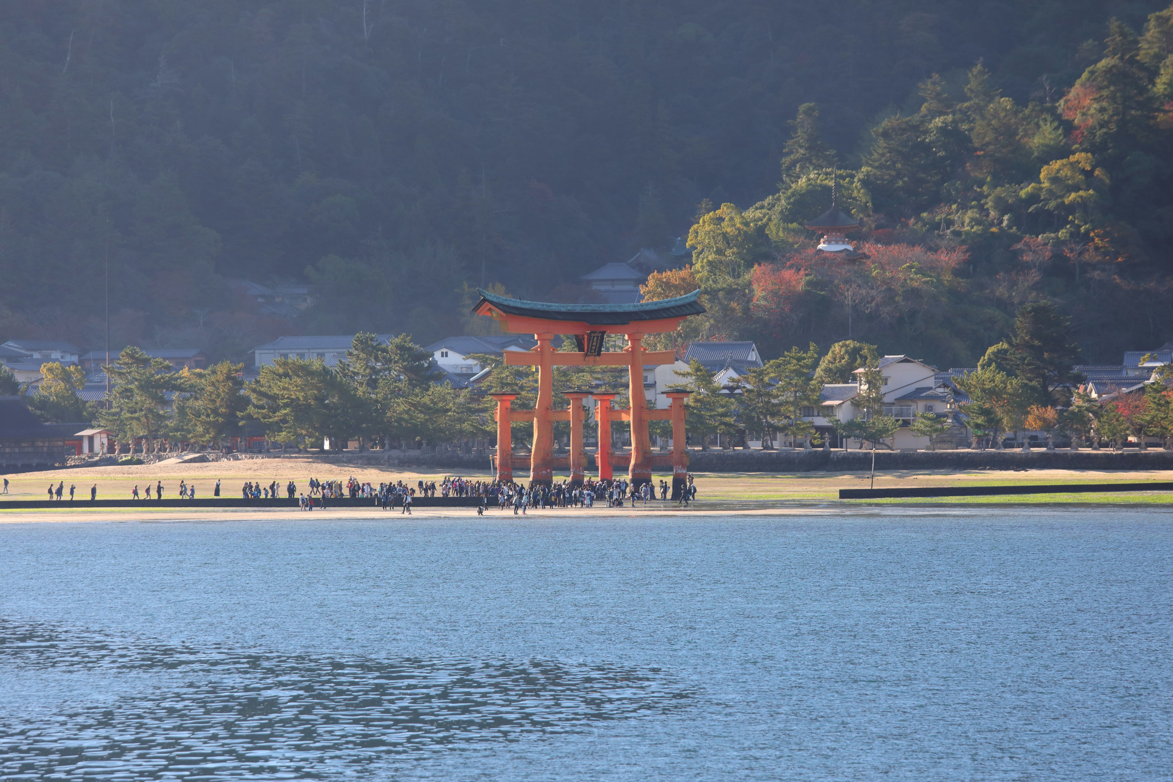 A large red torii gate near the water with mountains in the background