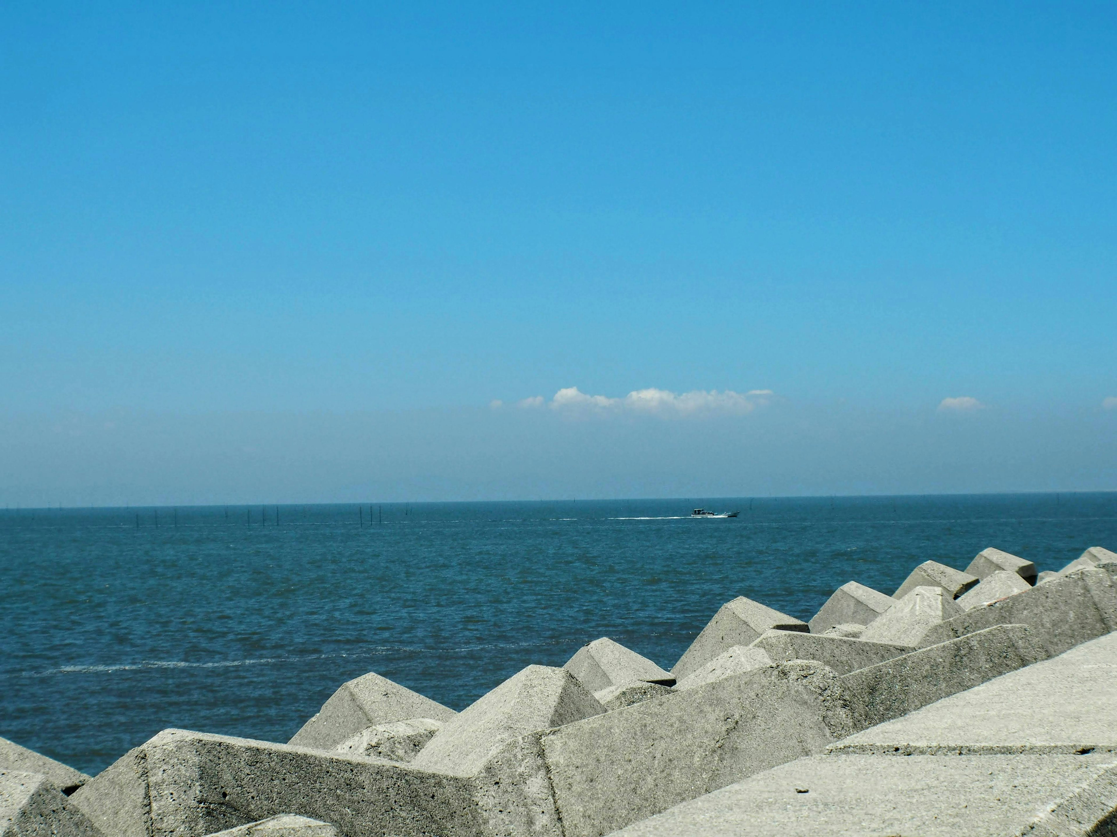 青い海と空の風景にコンクリートの防波堤が並ぶ