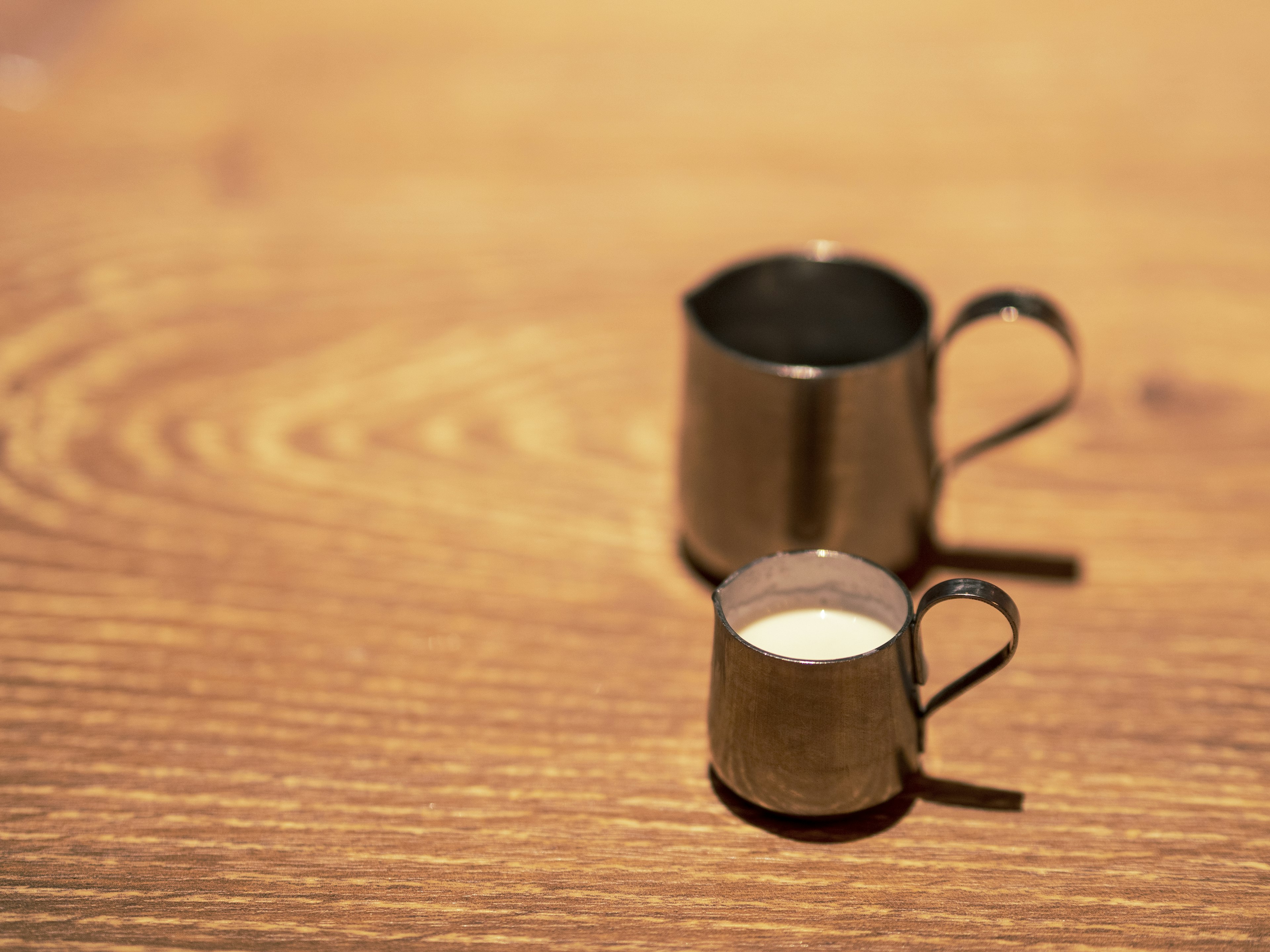 Un piccolo bricco di latte in metallo accanto a un bricco di latte in metallo più grande su un tavolo di legno