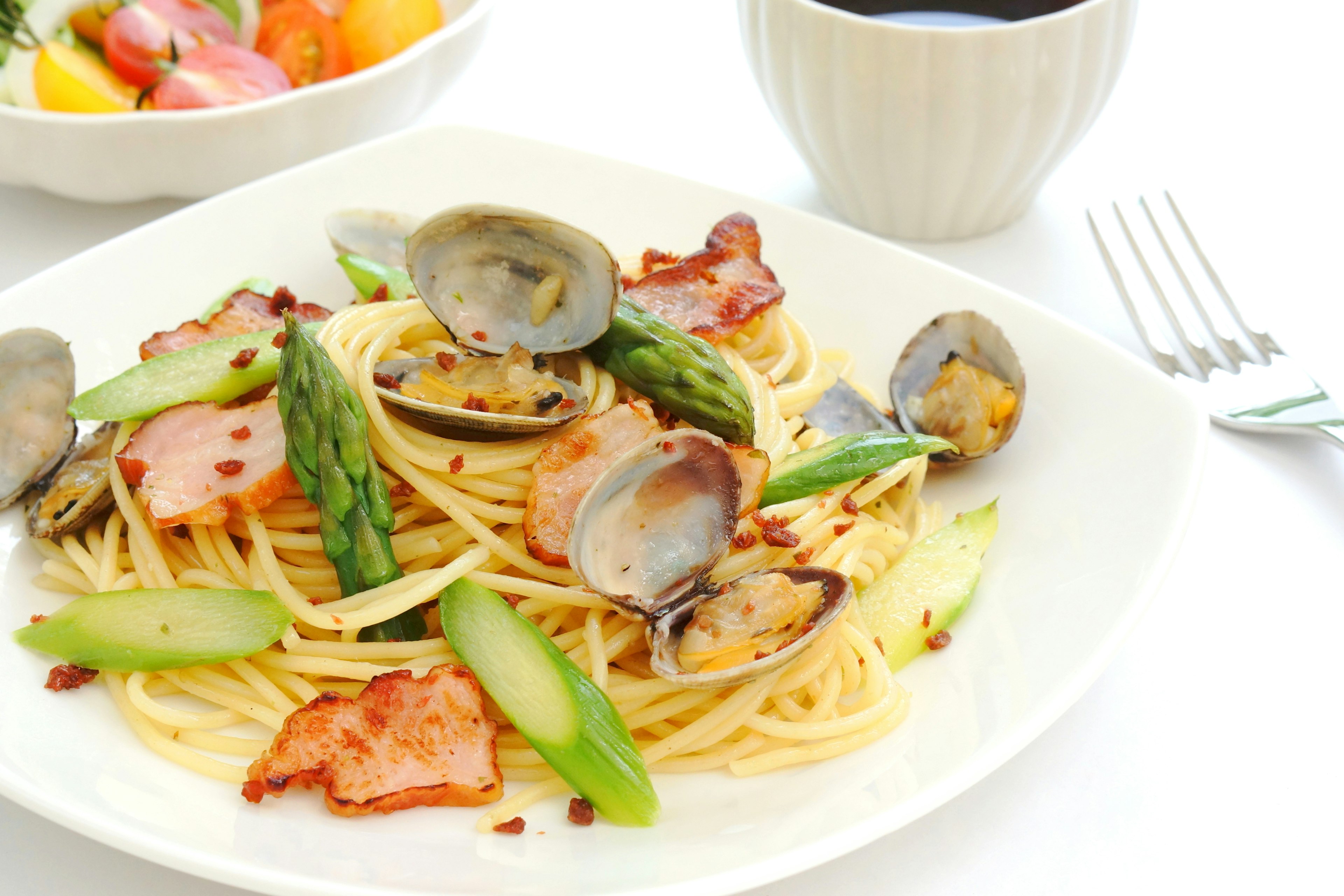 Assiette de spaghetti garnie d'asperges, de jambon et de palourdes