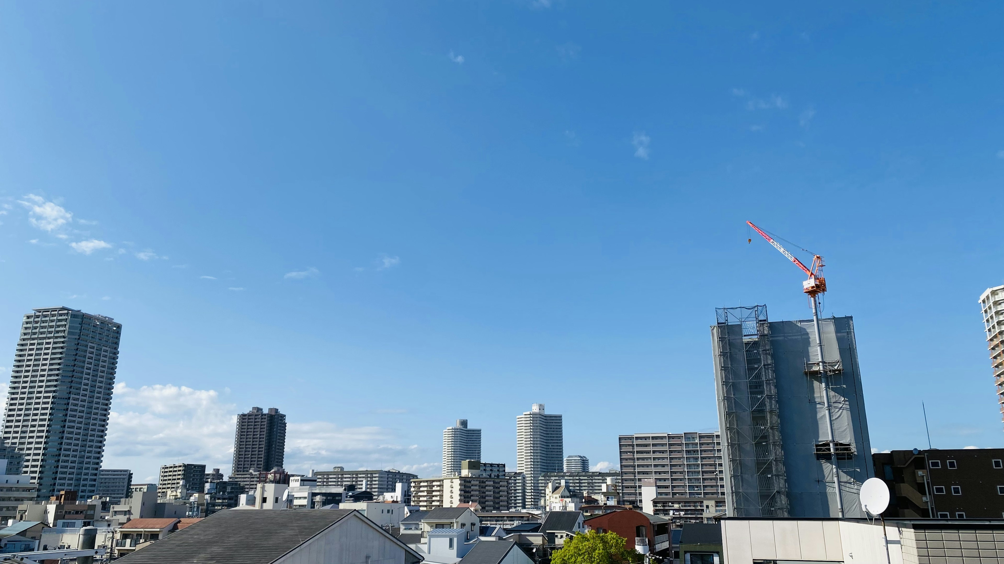 青空の下に広がる都市の風景 高層ビルと建設クレーンが見える