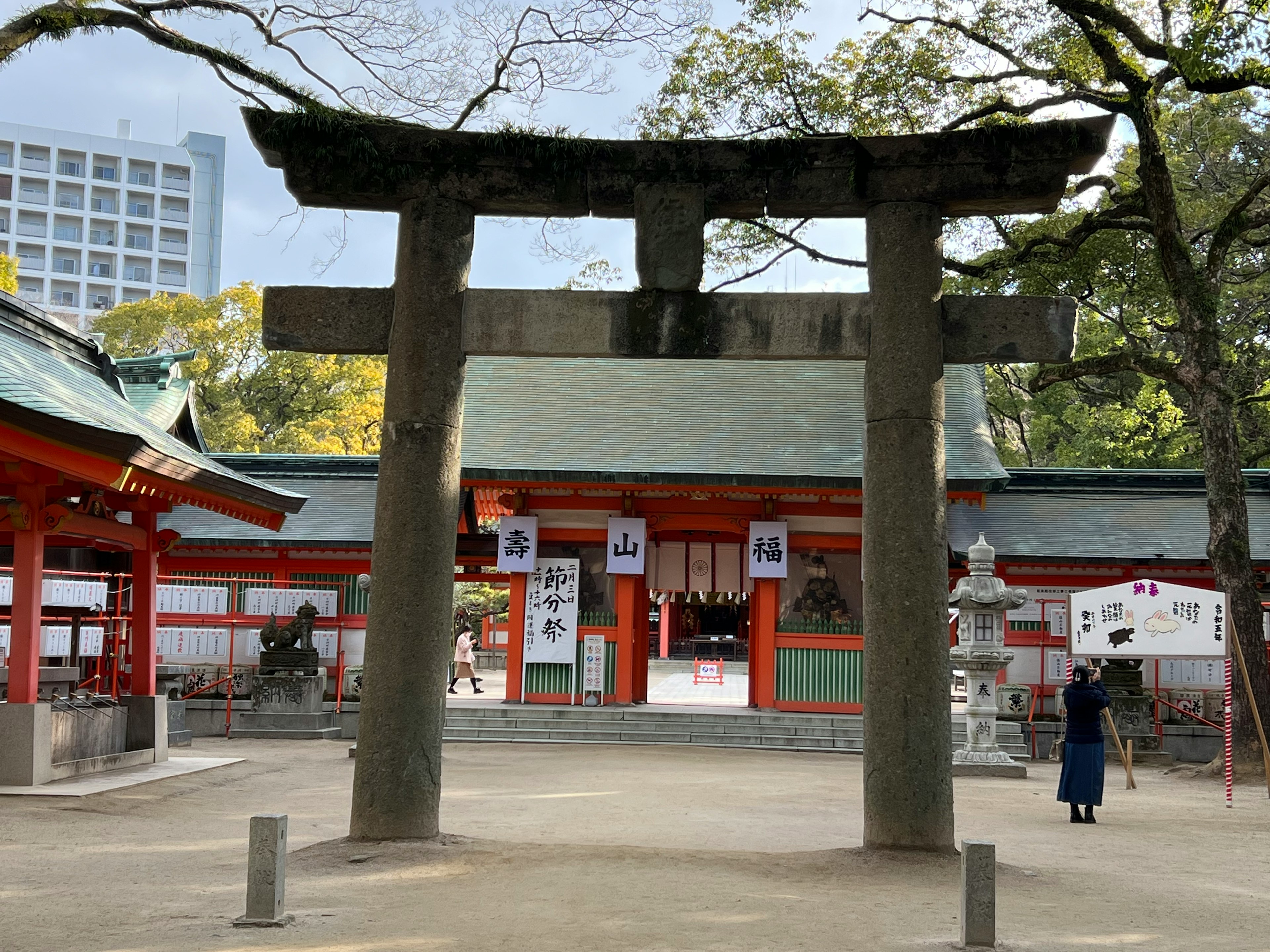 Puerta torii de piedra frente a un santuario sintoísta con un visitante