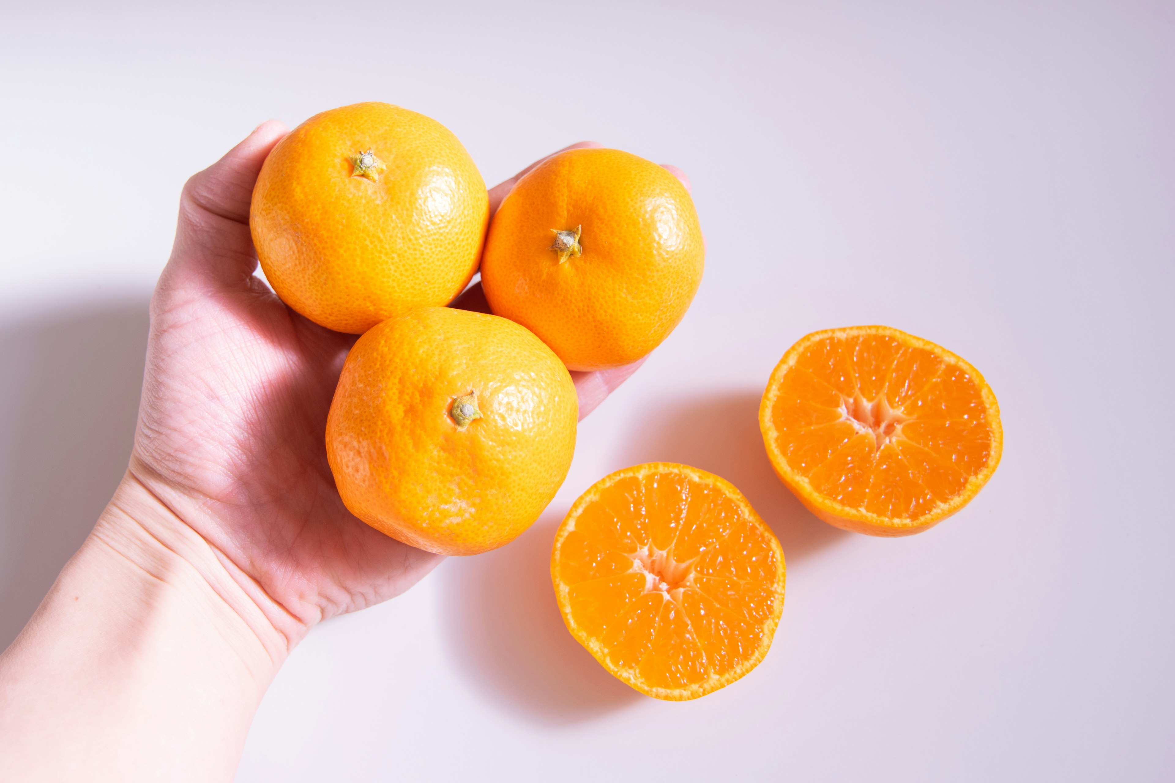 Hand holding three bright orange mandarins and two halved mandarins on a light background