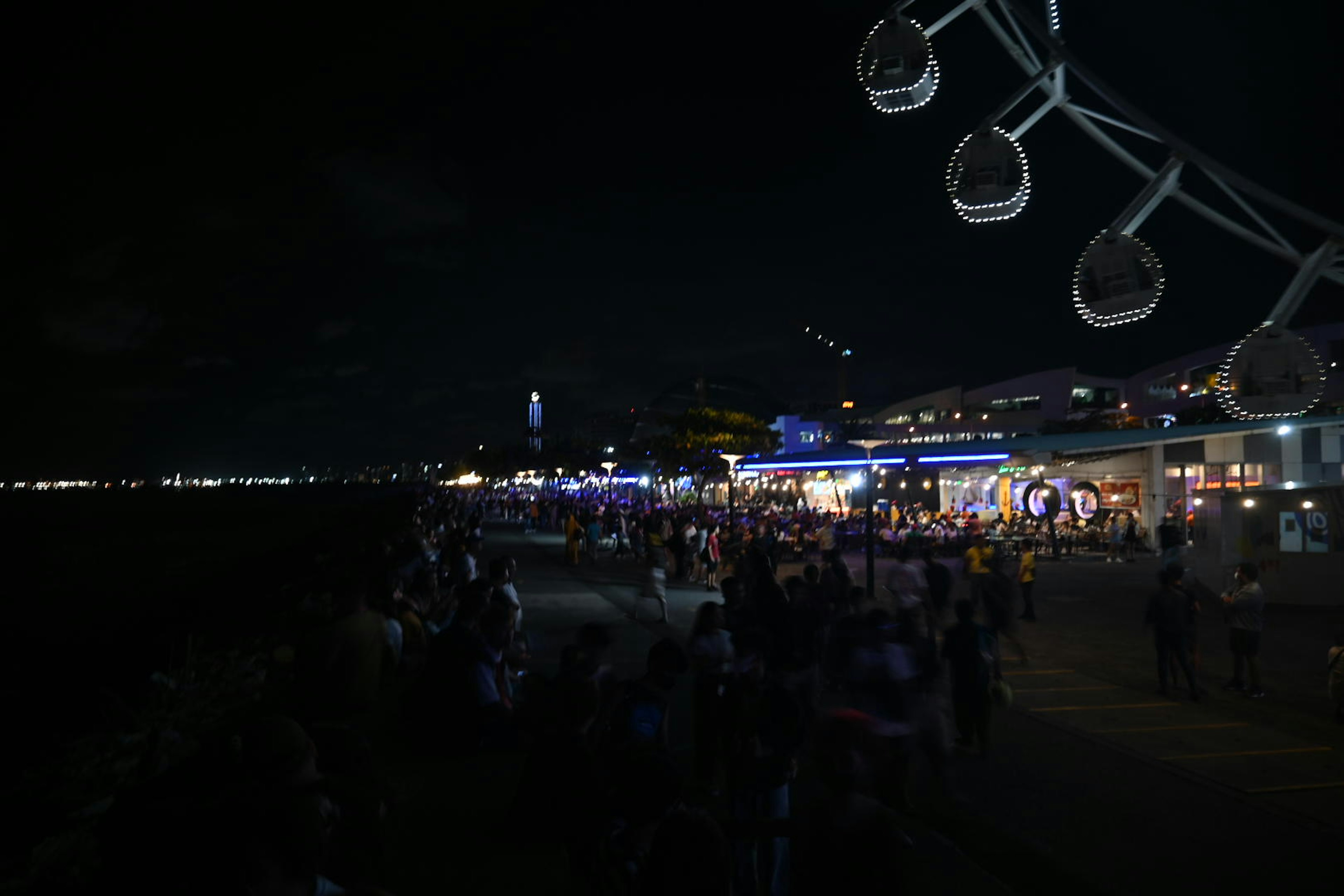 Multitud reunida a lo largo del paseo marítimo por la noche con iluminación azul