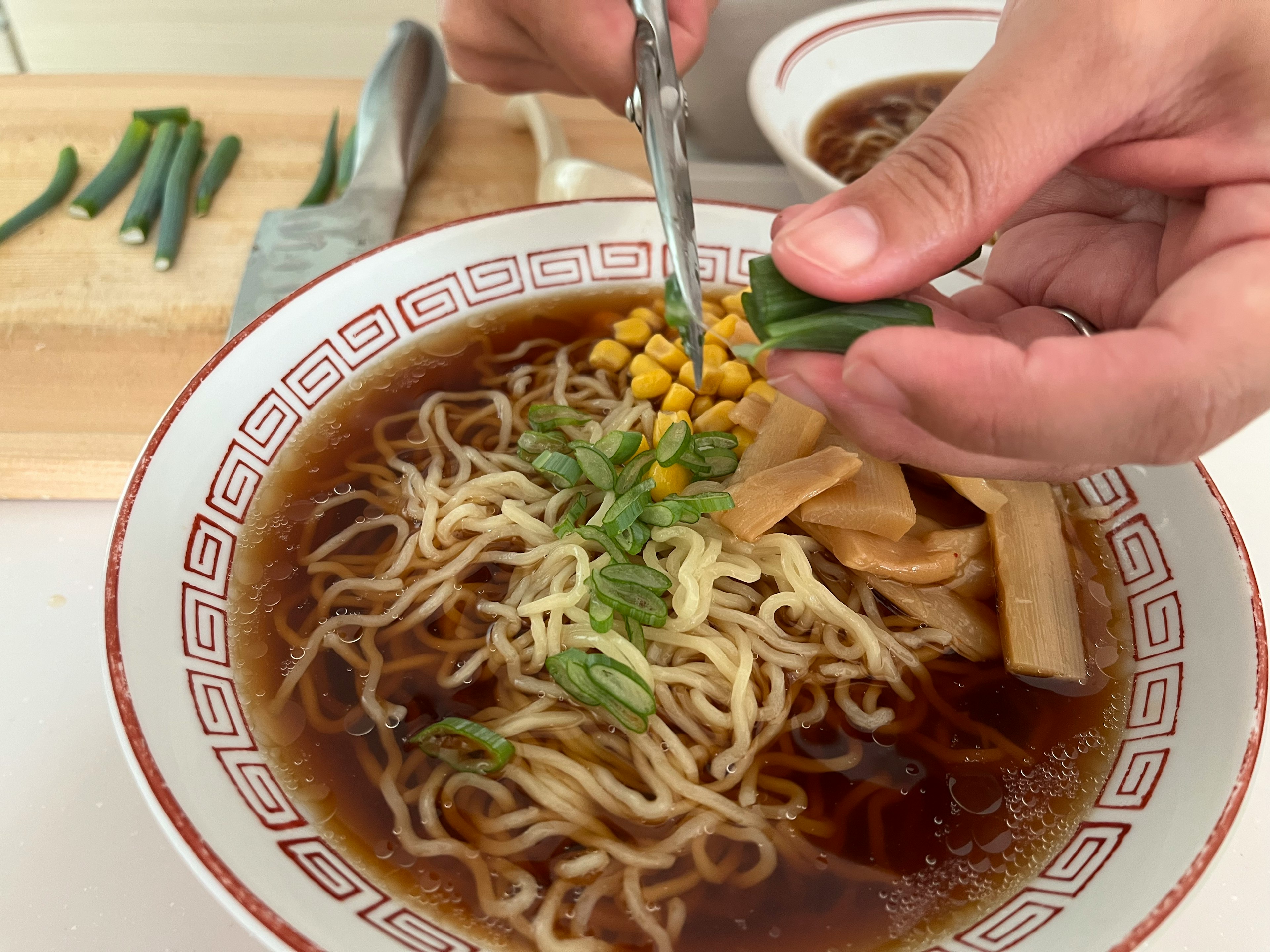 Ramen bowl being garnished with green onions by hand