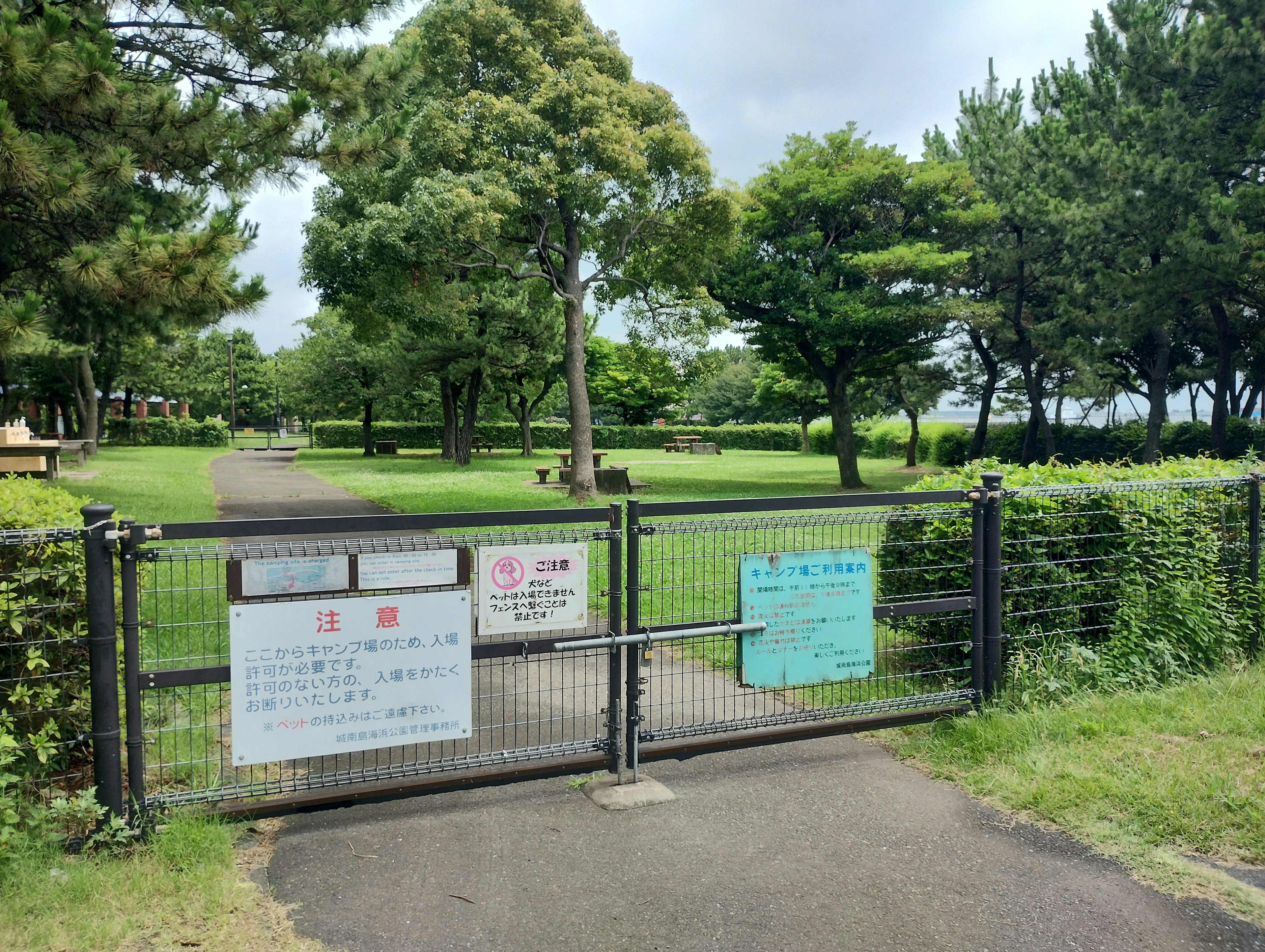 Closed gate to a park featuring green grass and trees