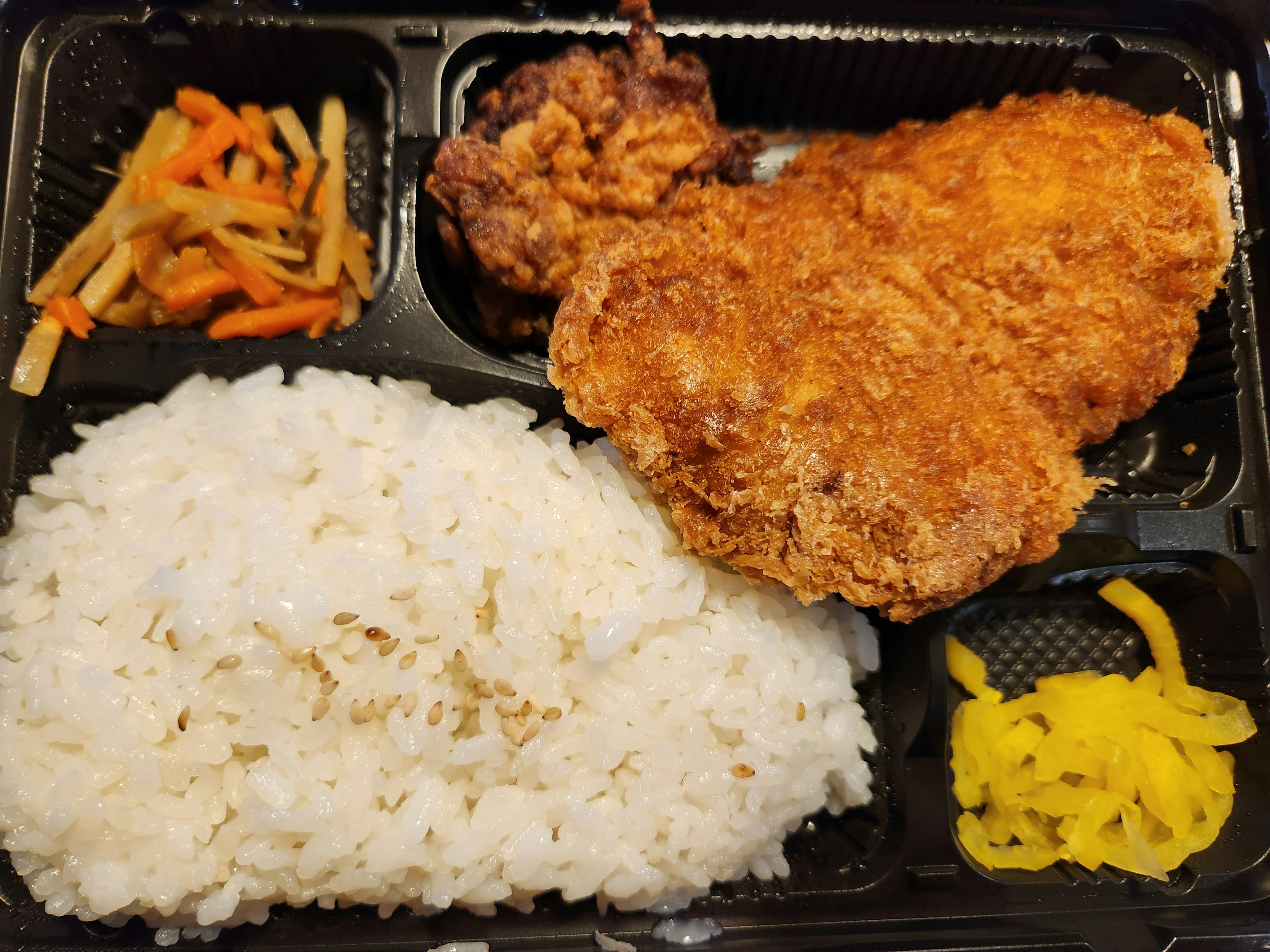 A bento box featuring fried chicken rice pickled vegetables and colorful sides