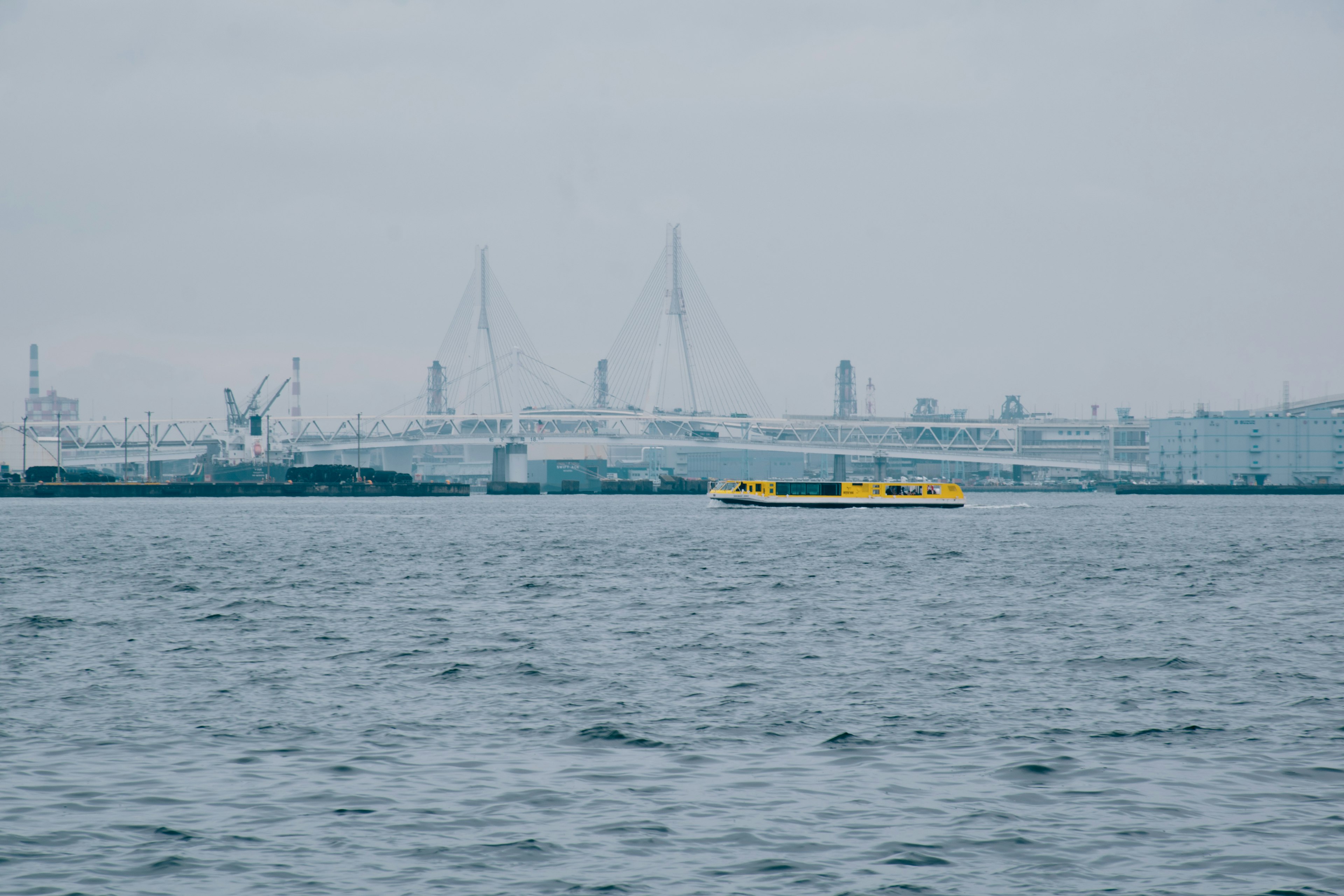 Yellow boat floating on the sea with an industrial area in the background under a cloudy sky