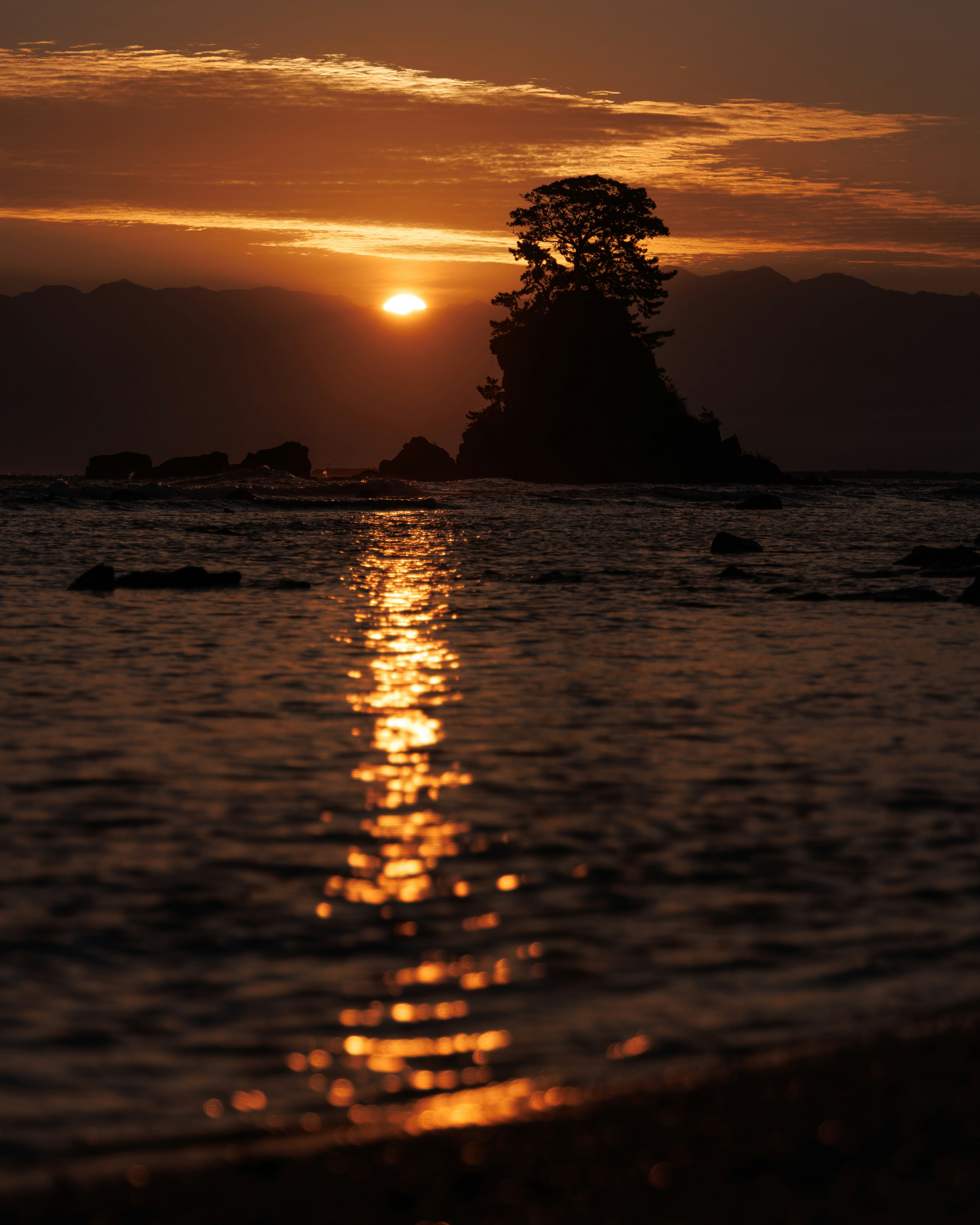 Silhouette eines einsamen Baumes auf einer kleinen Insel bei Sonnenuntergang über dem Ozean