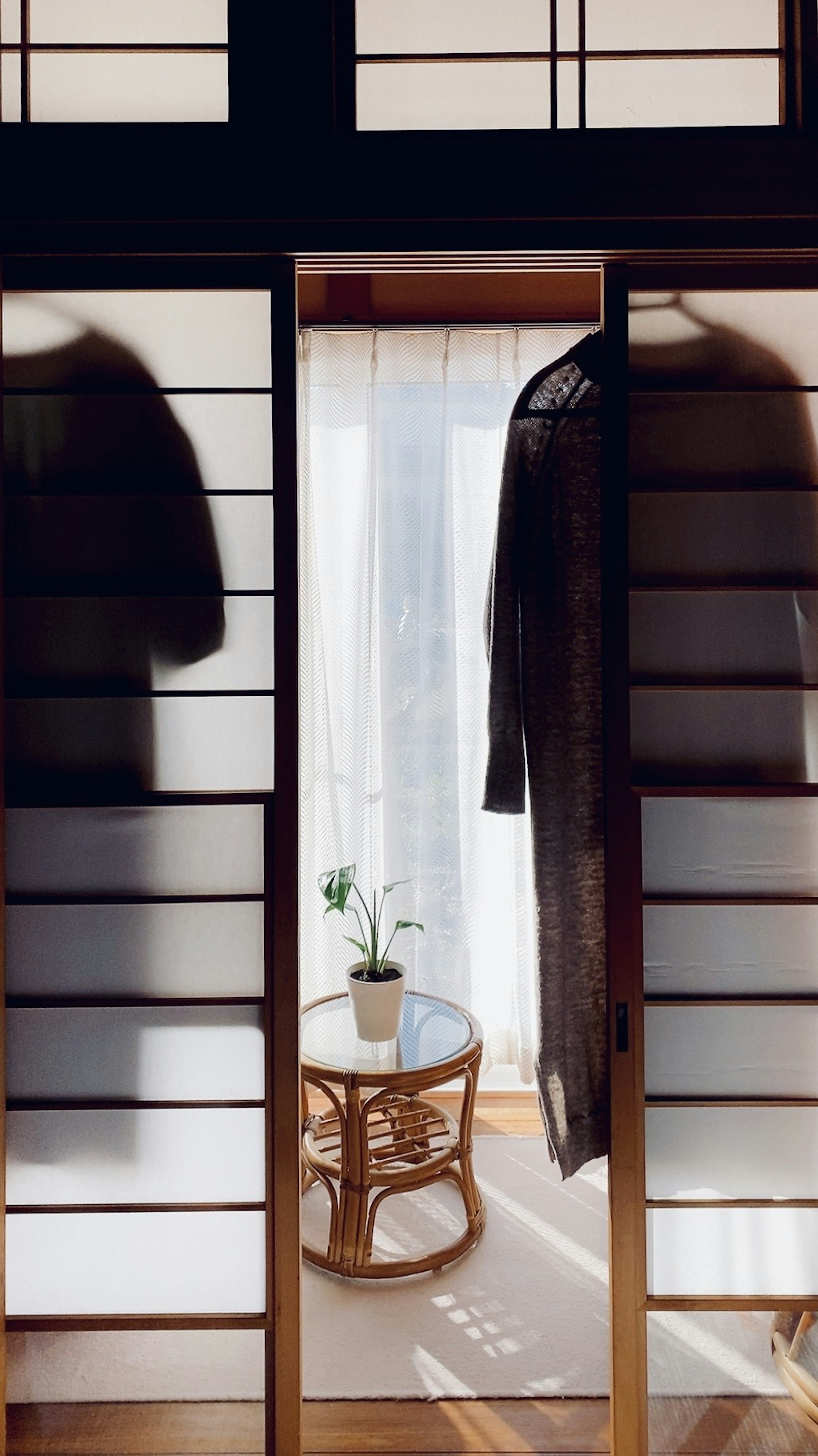 A serene view through shoji doors featuring hanging garments and a small table