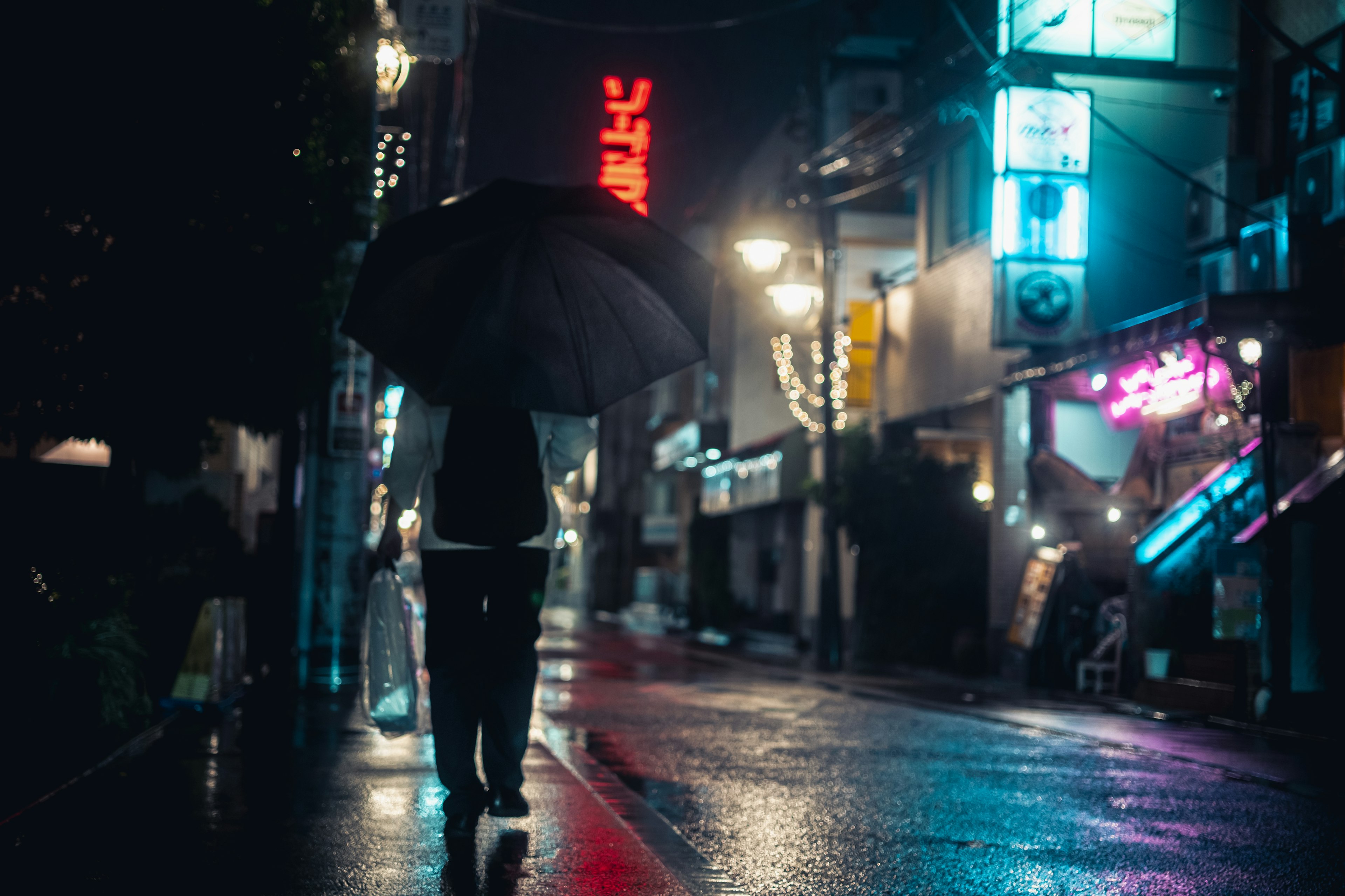 Person läuft mit einem Regenschirm im Regen Neonlichter in einer Nachtstadt