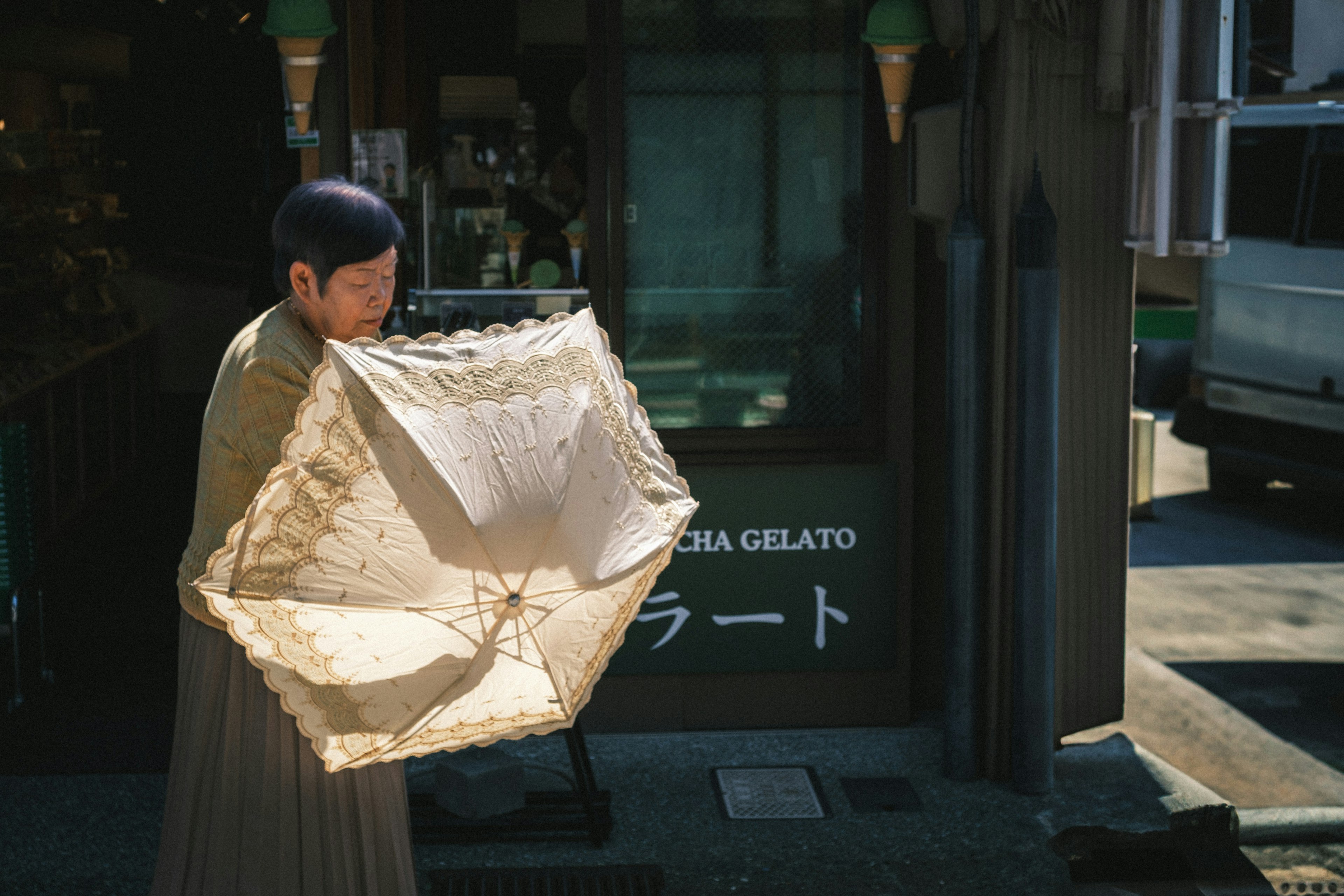 Personne tenant un parapluie blanc devant une boutique de gelato