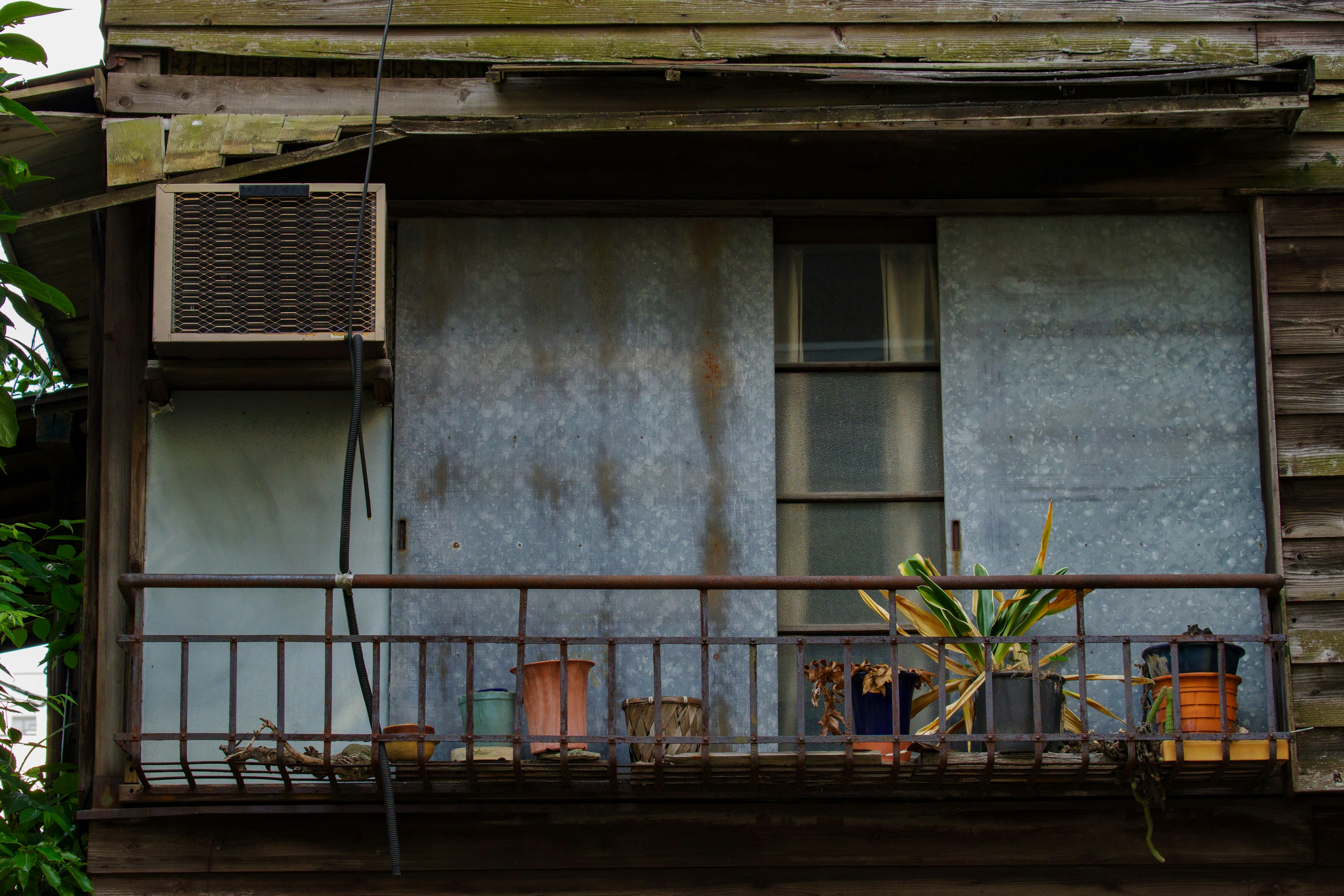 An old wooden building balcony featuring an air conditioning unit and potted plants