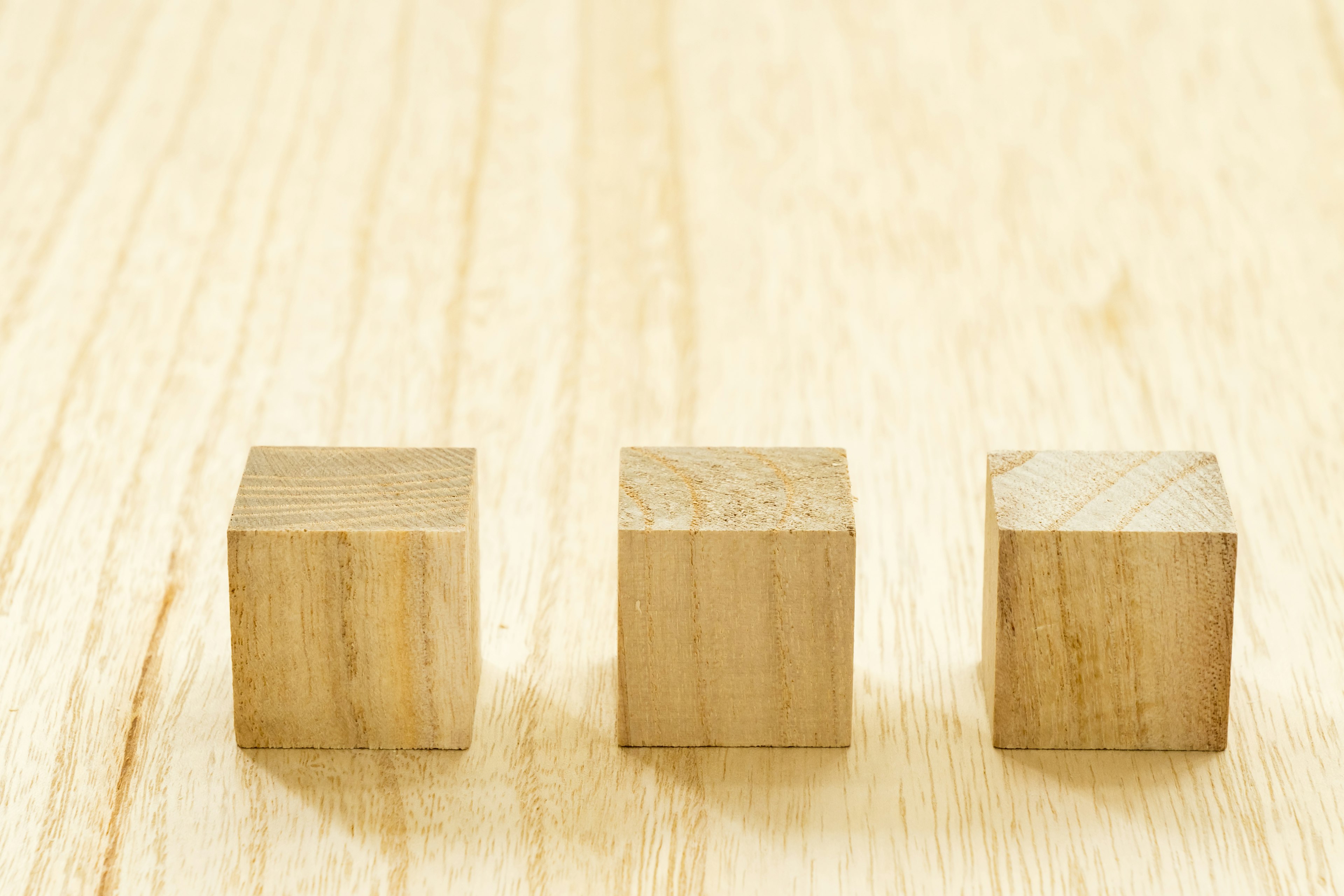 Trois cubes en bois alignés sur une surface en bois clair