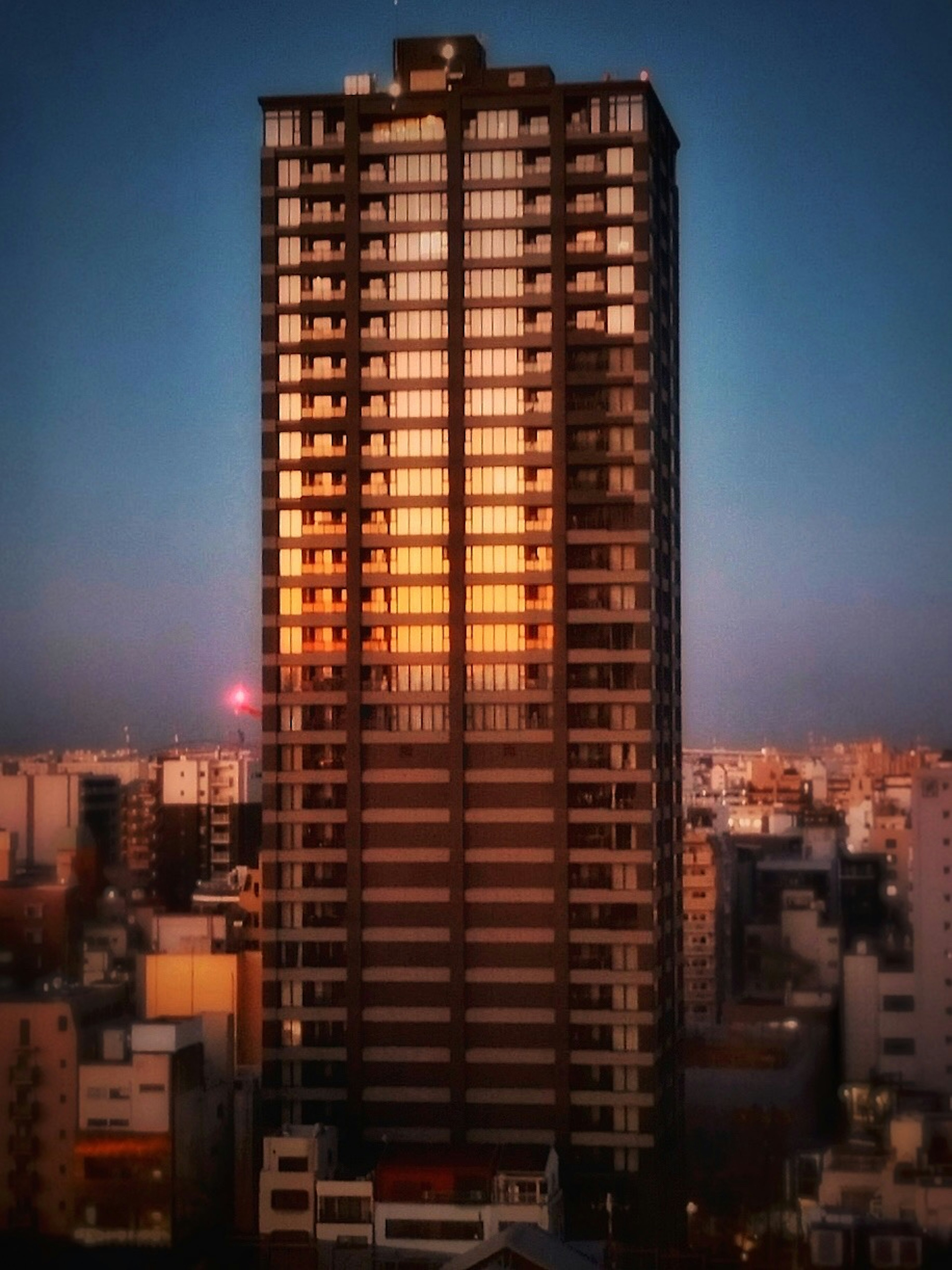 Image of a skyscraper reflecting sunset colors surrounded by urban landscape