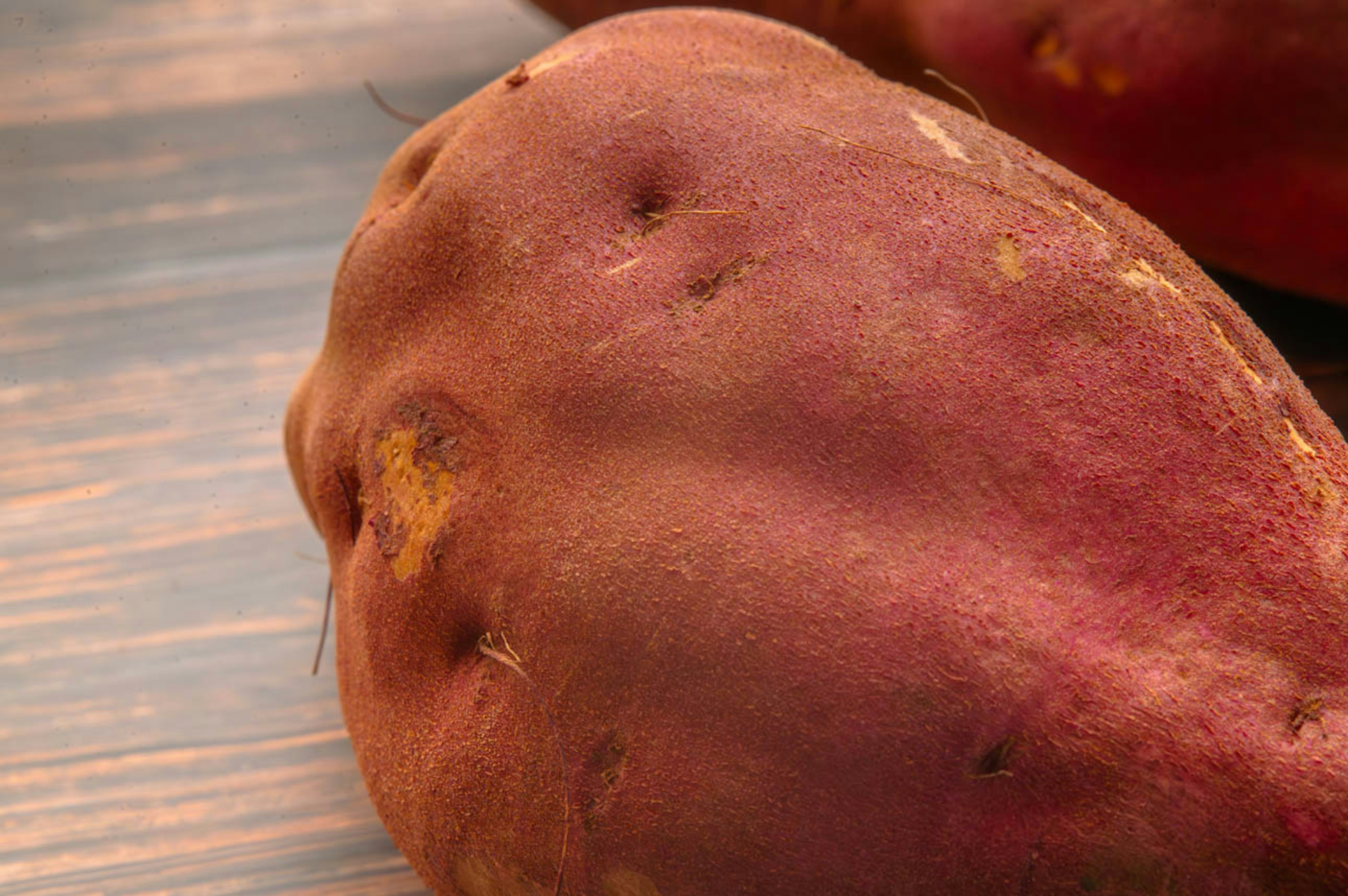 A close-up of a reddish-purple sweet potato on a wooden table