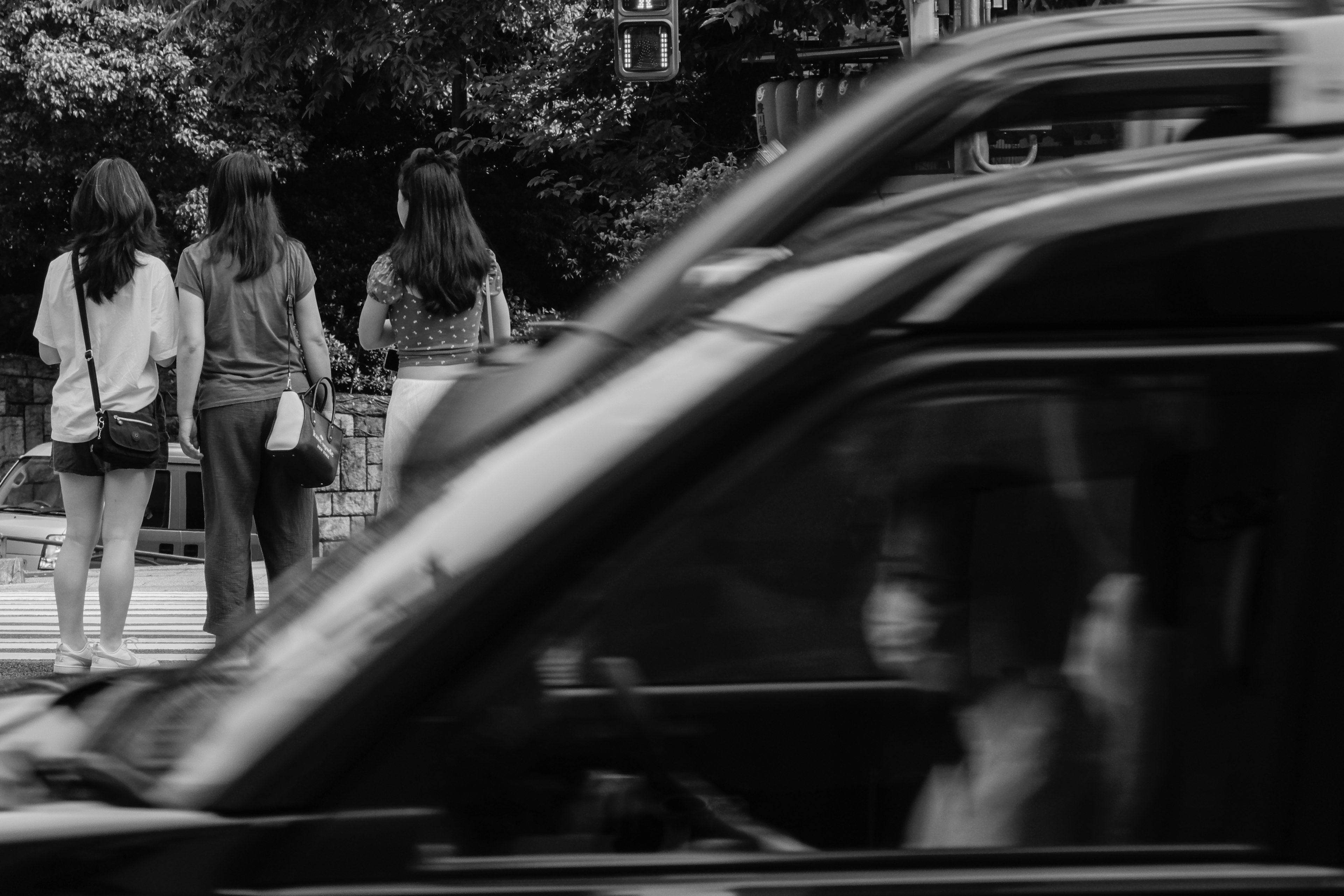 Black and white street scene with women walking on the sidewalk and a passing car